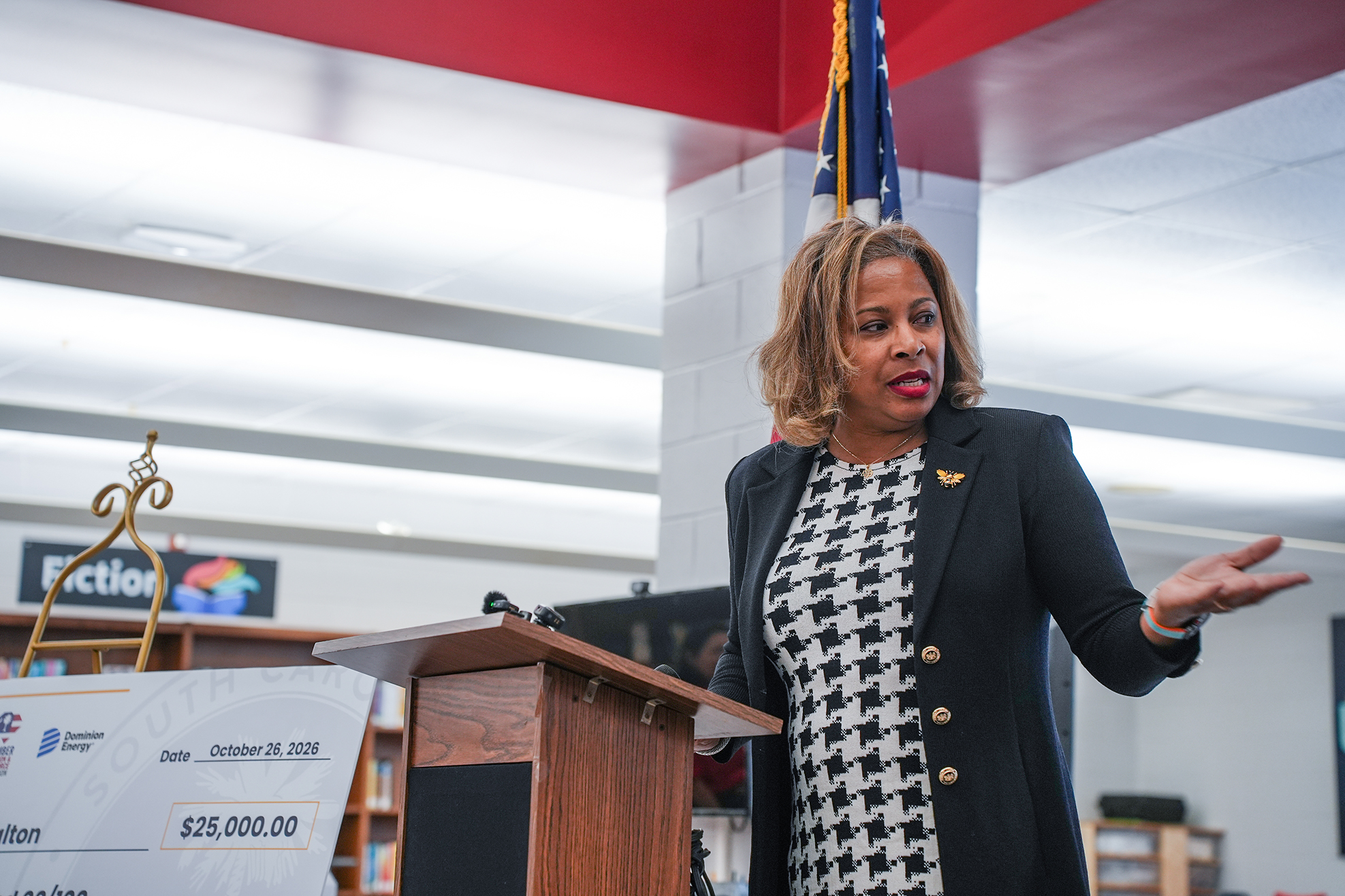 A woman speaks at a podium. Behind her is a banner with $25,000.00 written on it.