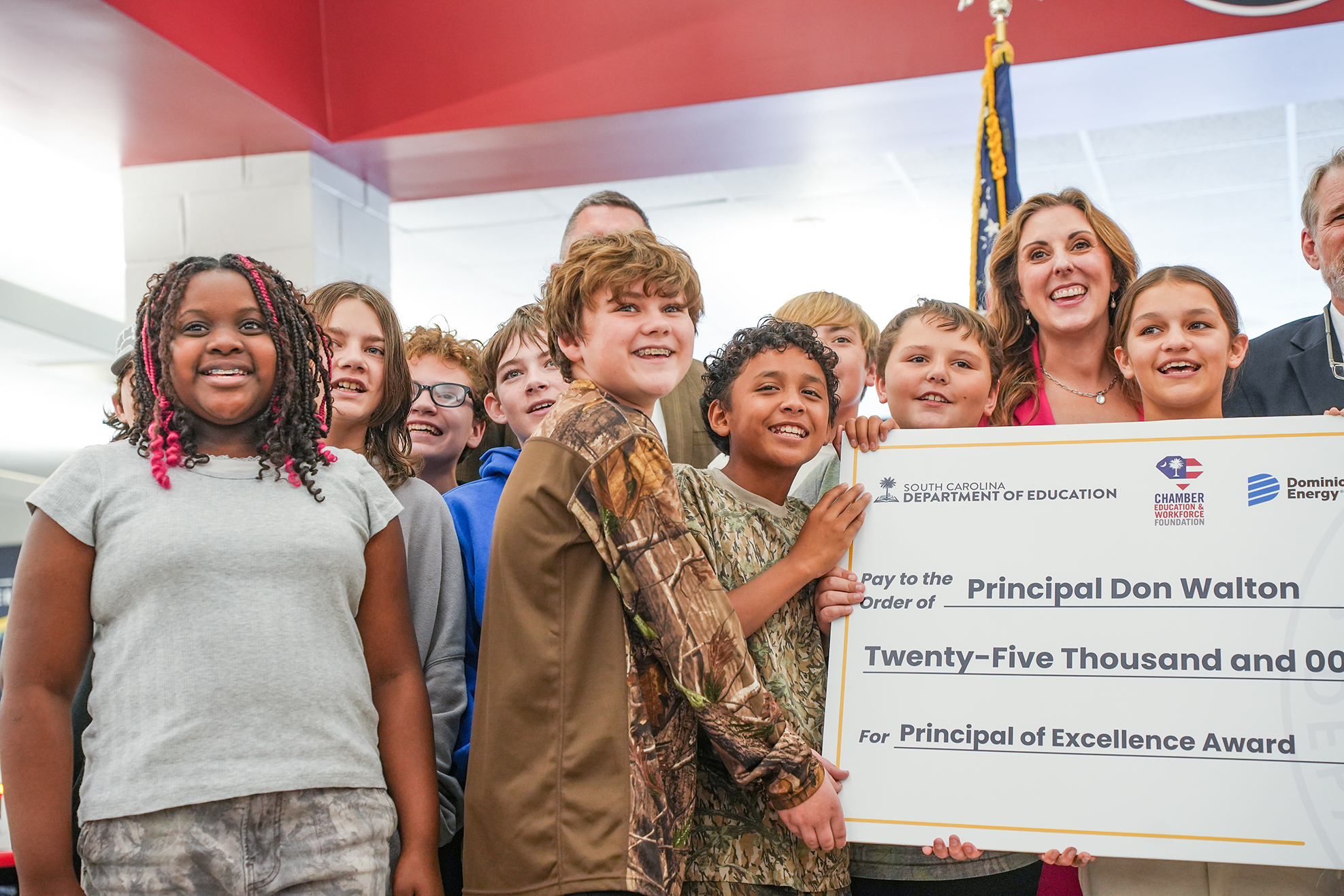 Group of students and adults holding a large check. One child holds the check in front of their chest.