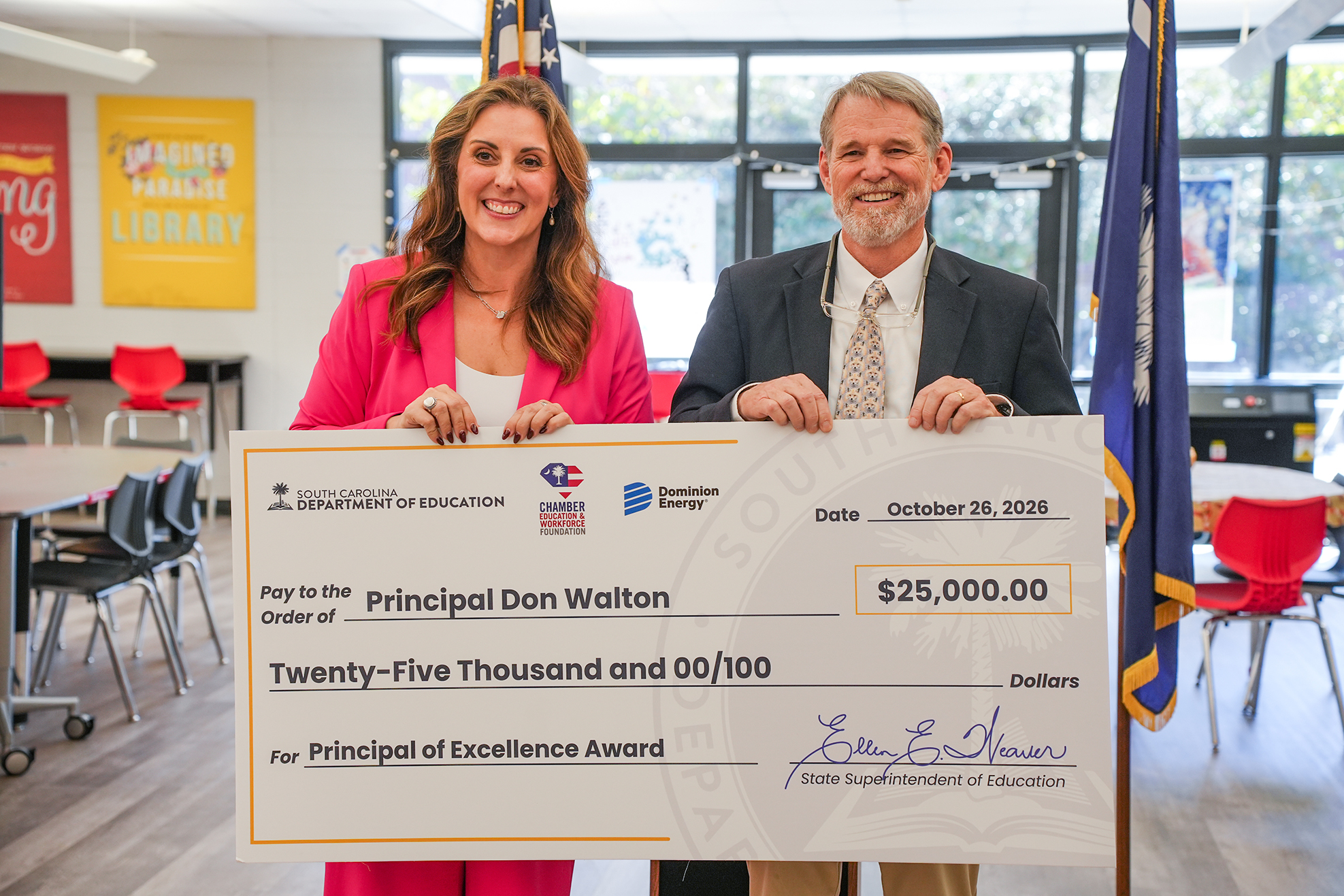 Principal and assistant principal holding a large check with a crowd of students in the background.