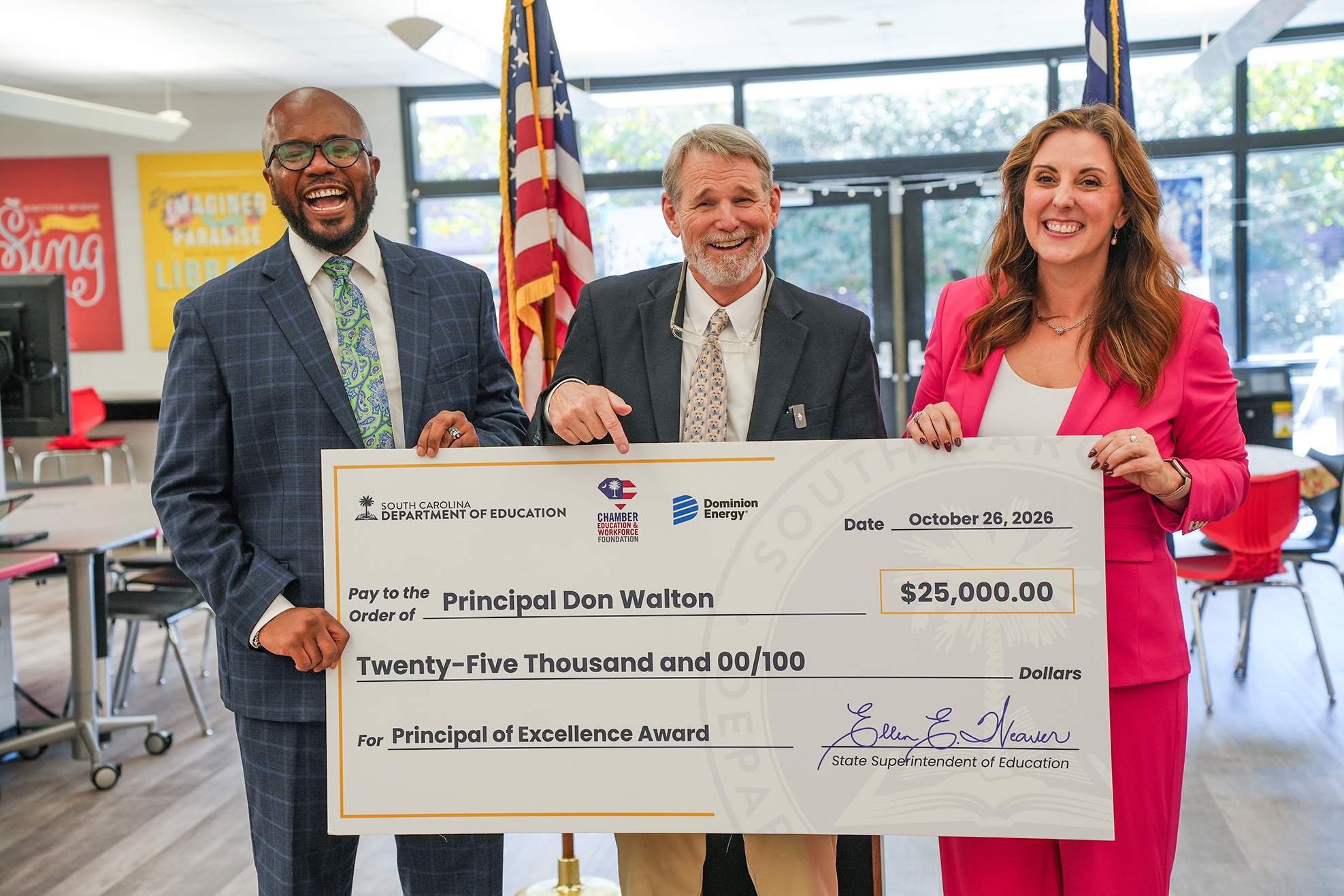 Three adults stand behind a large check for $25,000, smiling and holding it up for a photo.