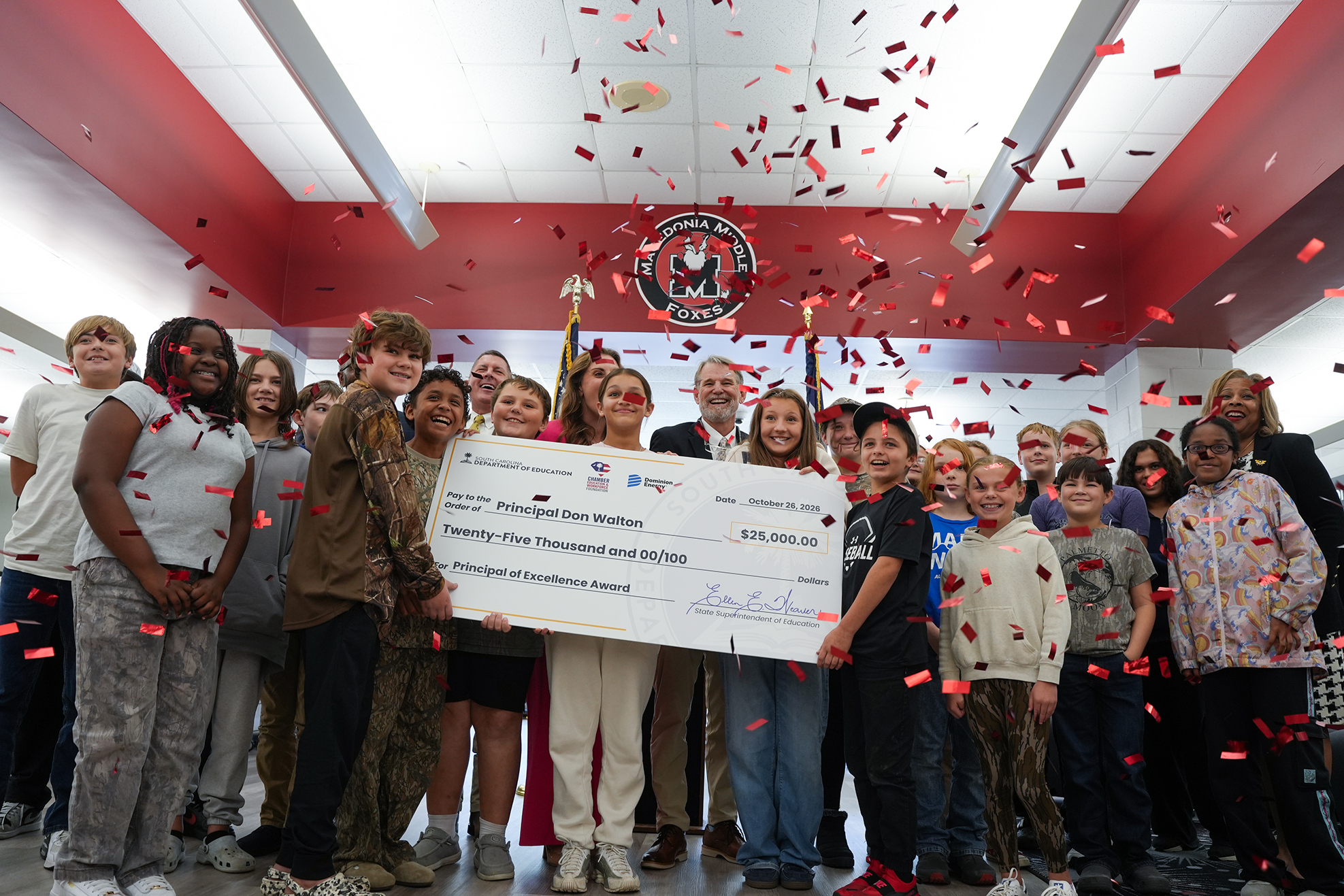 Confetti falling as a group of children and adults hold a check above their heads.