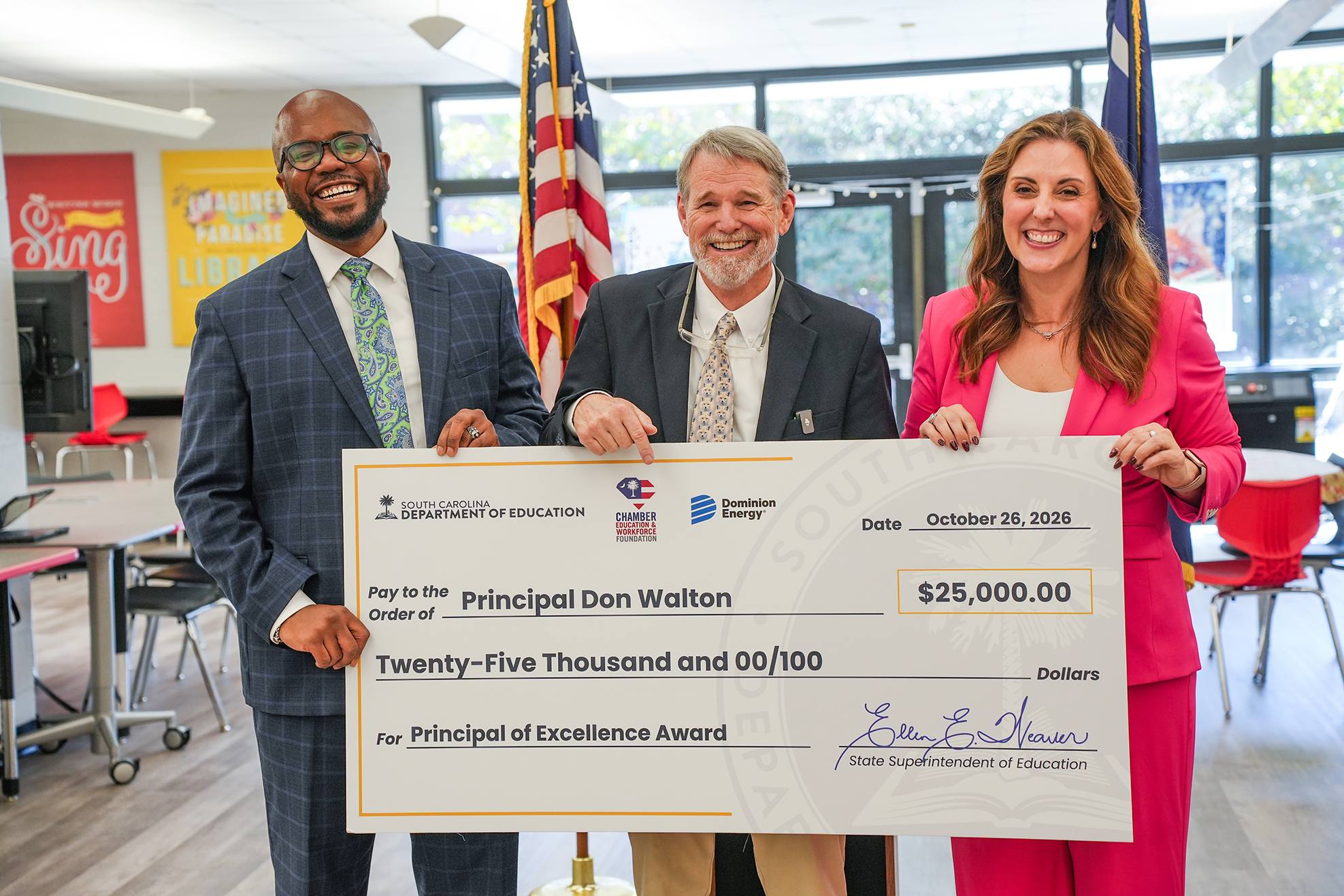 Three people holding a large check. Two men and a woman in business suits and ties.