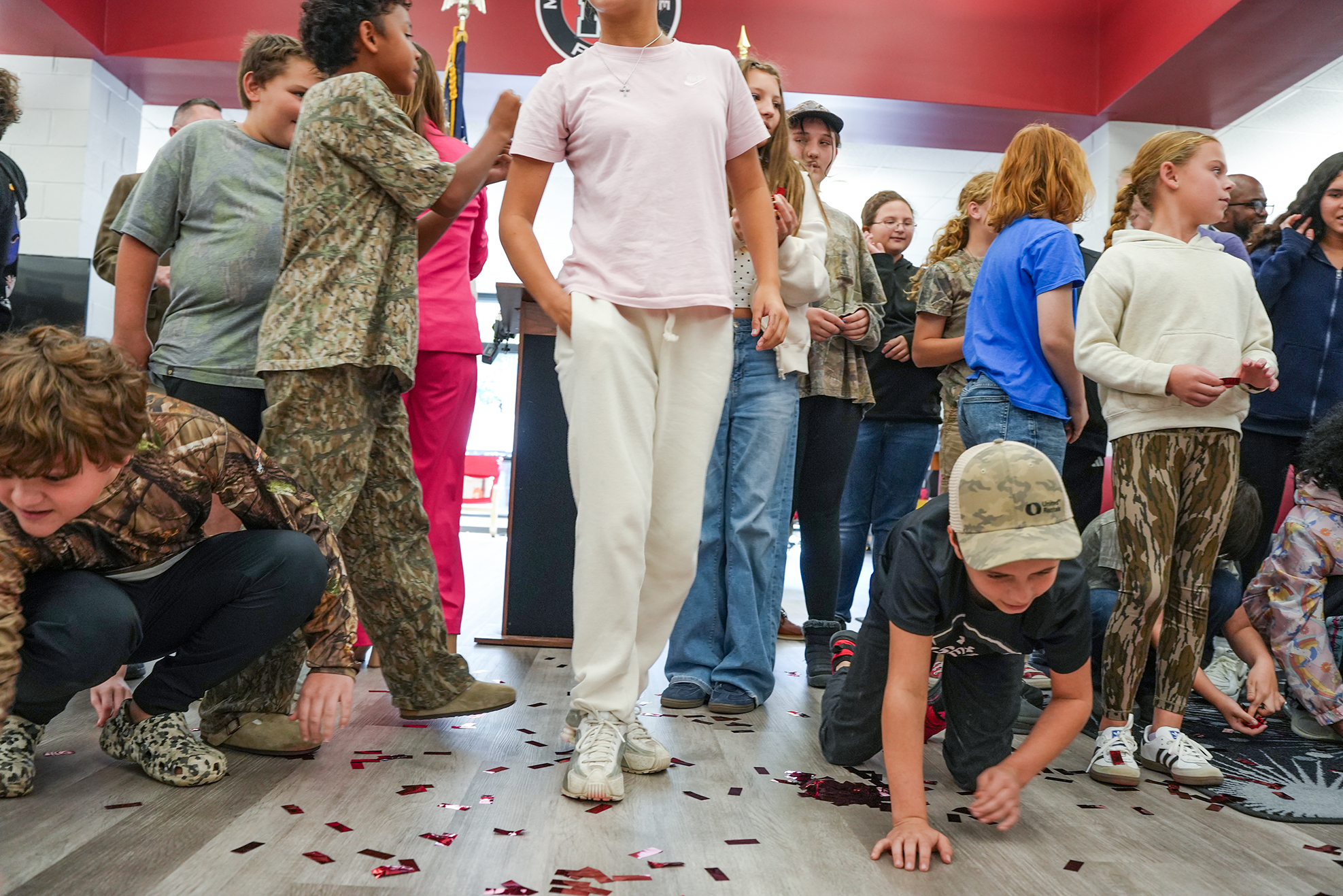 Group of students in a room with red walls and red petals on floor, some kneeling and others standing.