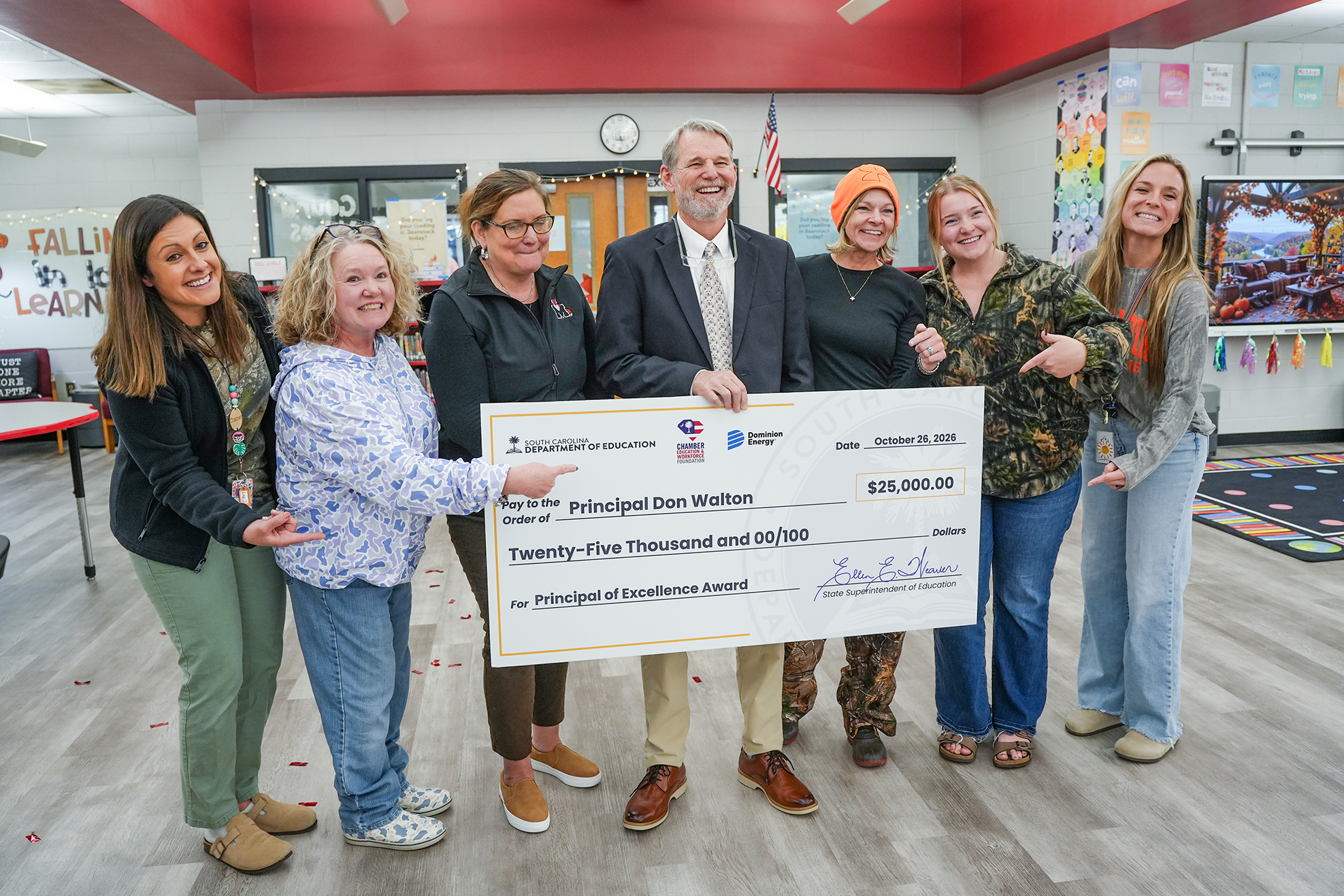People standing in a room, holding a large check, with one person pointing to the check.