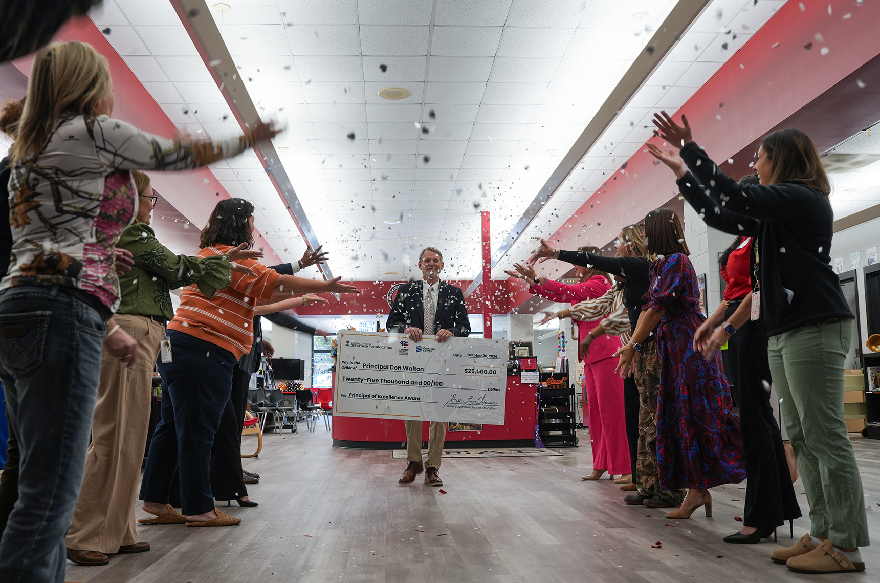 Several people raise hands in a room while a man stands with a large check.