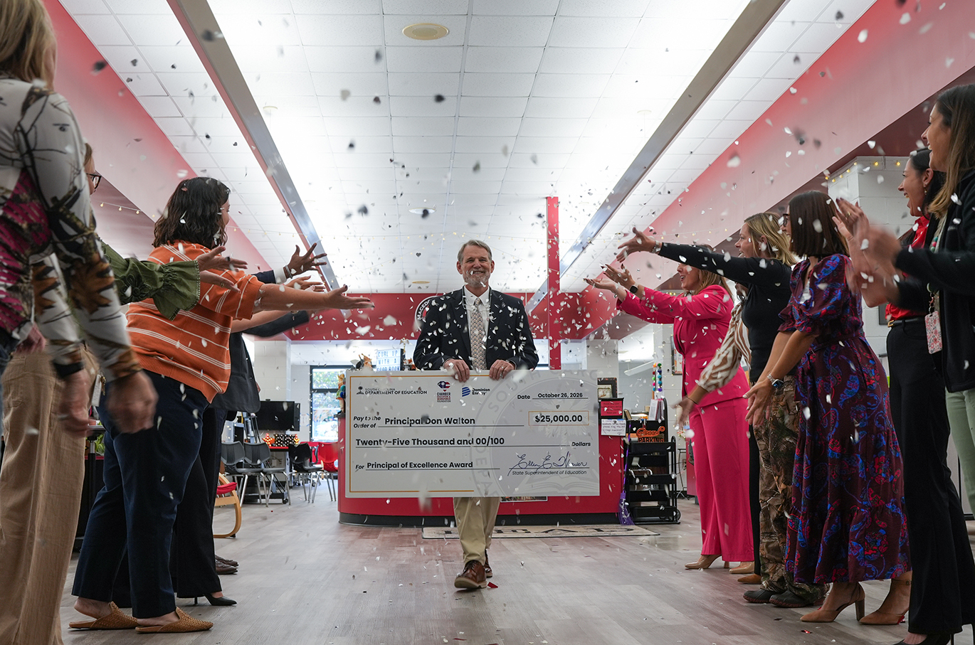 A man in a suit holds a large check while a crowd of people stand around him, clapping.