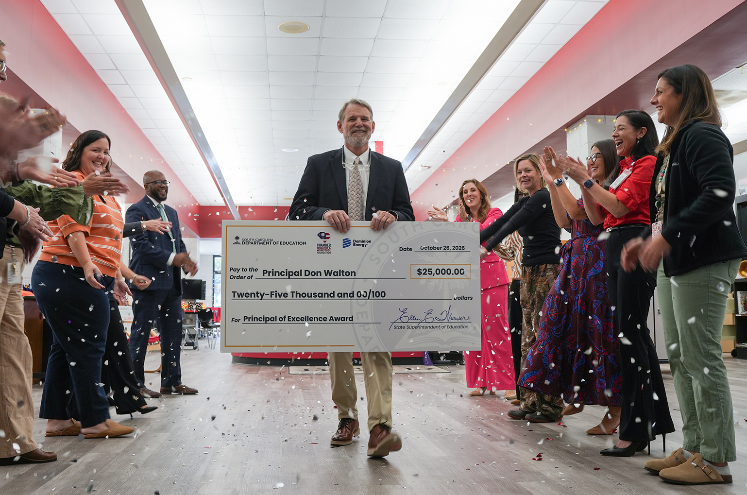 A man stands with a large check in his hands as people cheer and throw white confetti.