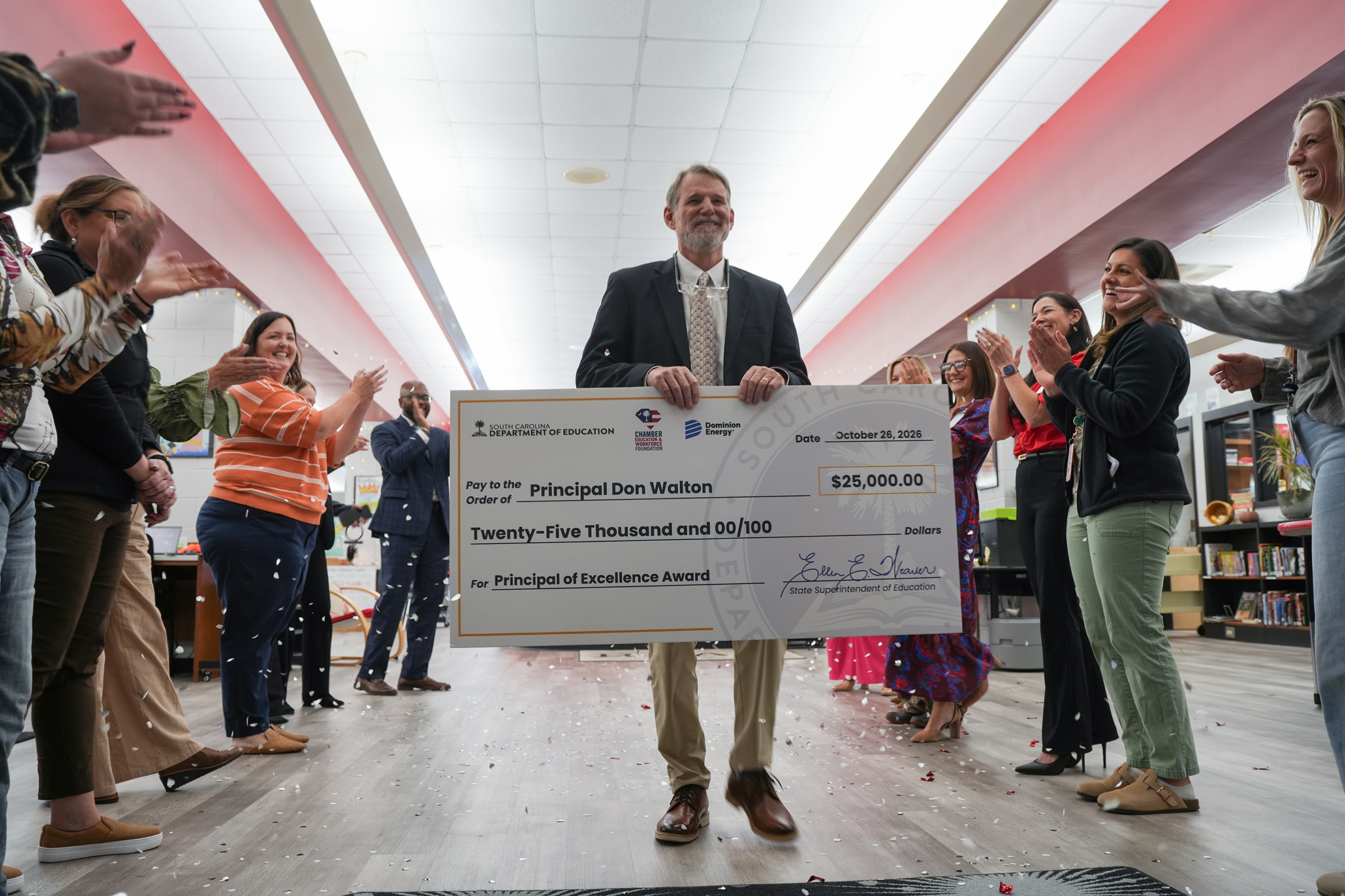 A group of people gathered around a person holding a large check. Some hold hands up.