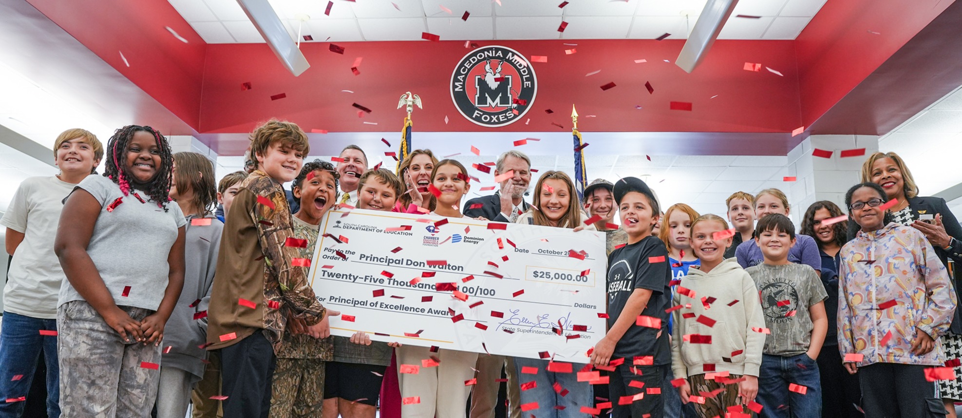 A group of people in a room holding a check, with red confetti falling in the background.
