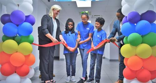 3 kids and two adults cutting opening ribbon