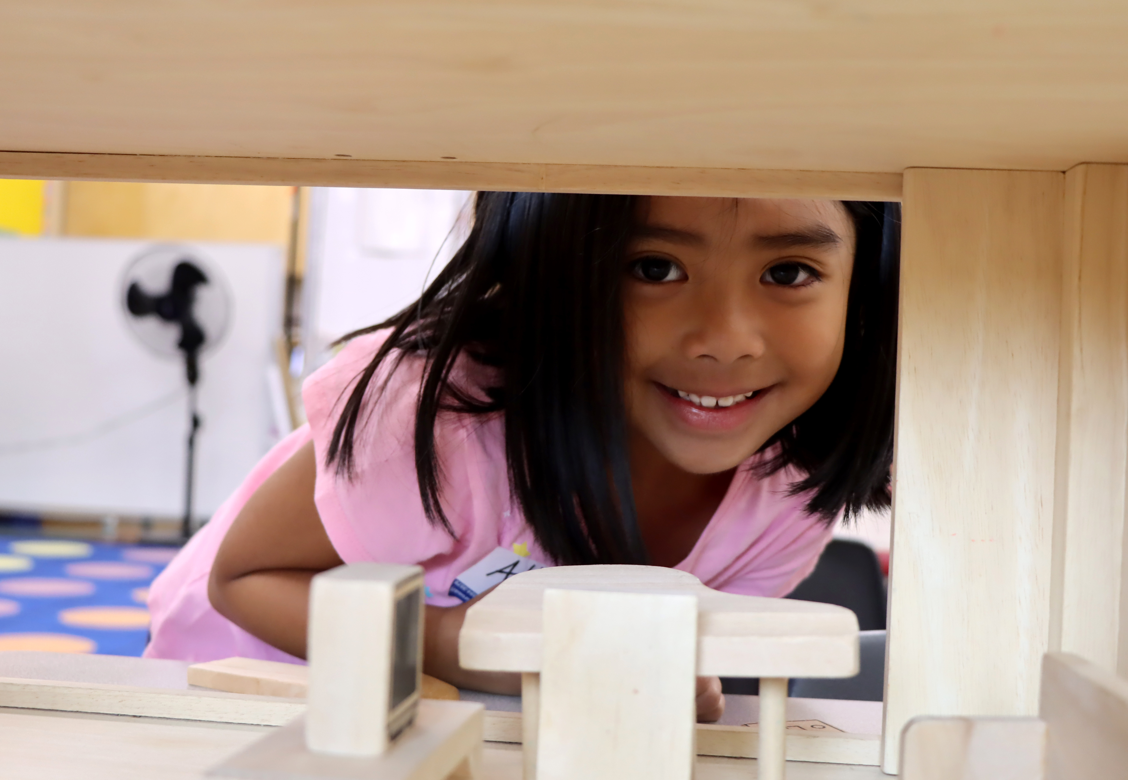 Young student peeking through a doll house