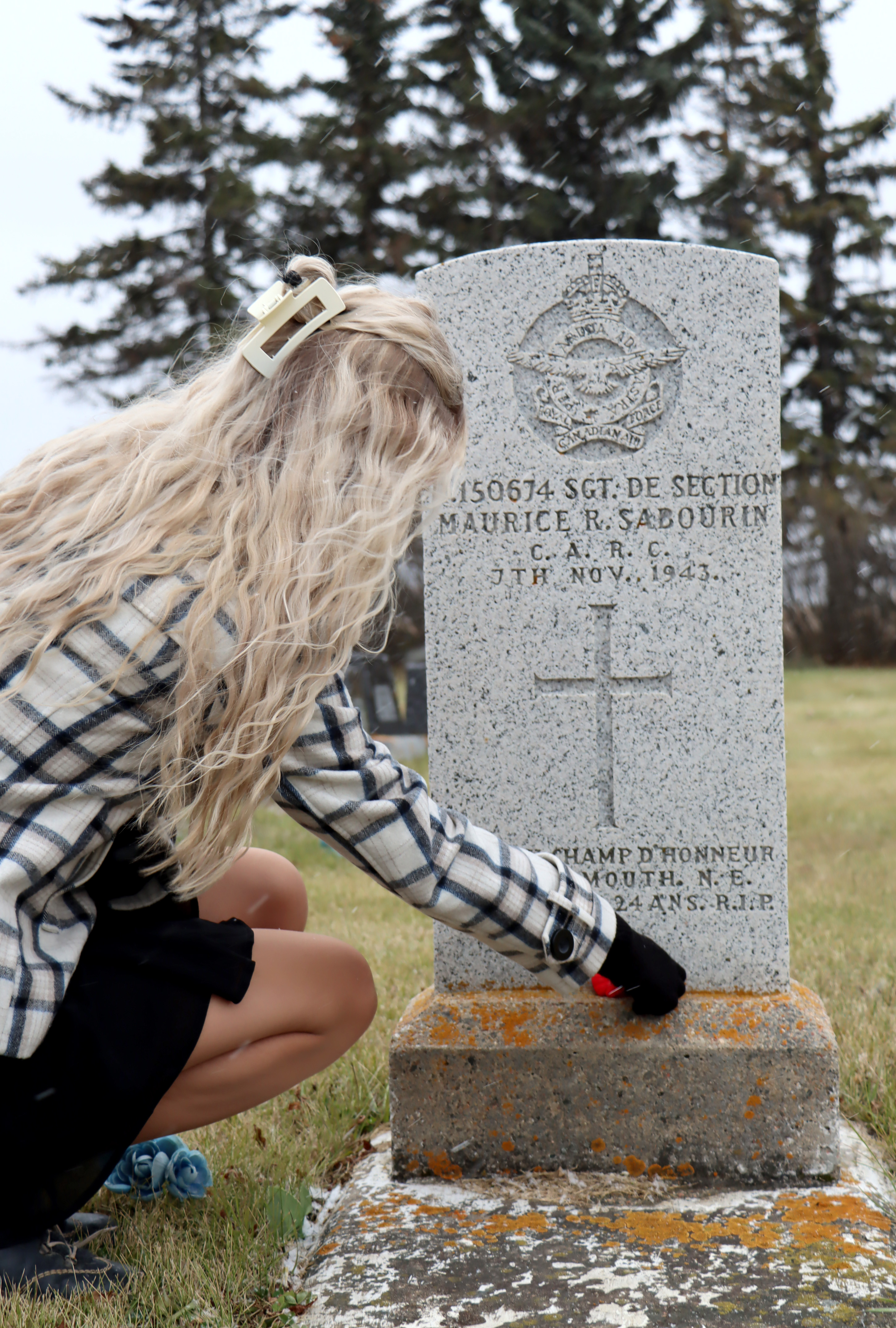 student placing poppy at headstone