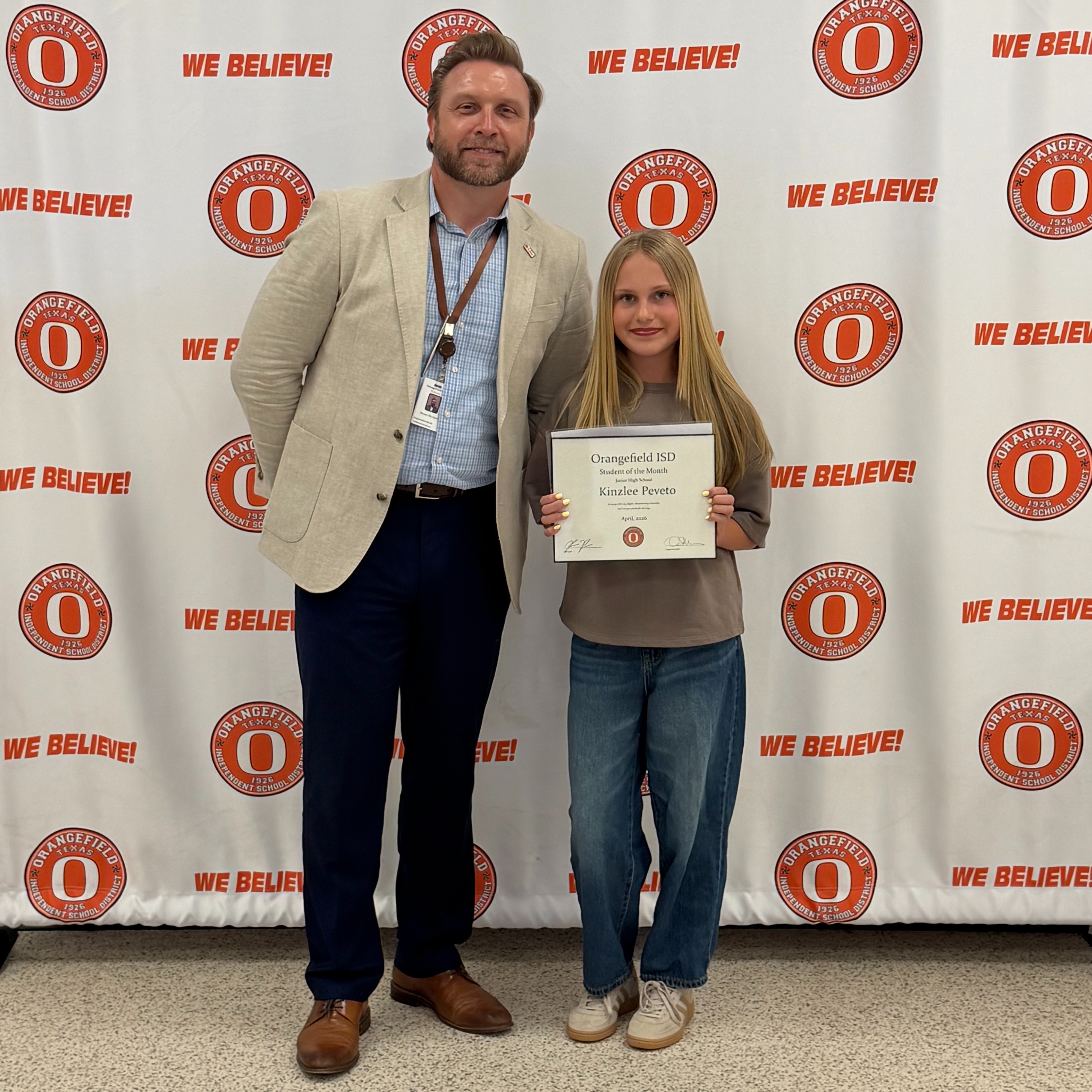 Man and girl stand in front of wall with orange circles, each holding a certificate, smiling.