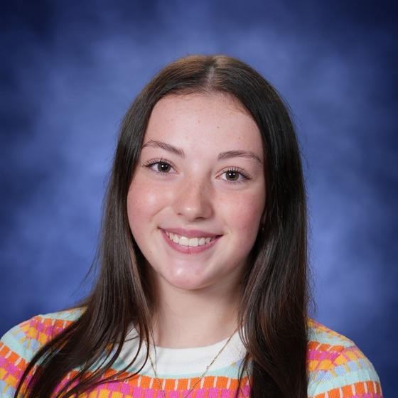 A girl with long hair wears a striped shirt with a necklace. She smiles and looks forward.