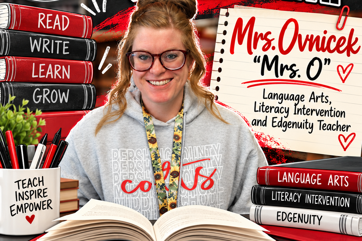 A smiling woman wearing glasses sits at a desk with books and a notebook. Behind her, a chalkboard displays "August Teacher of the Month".