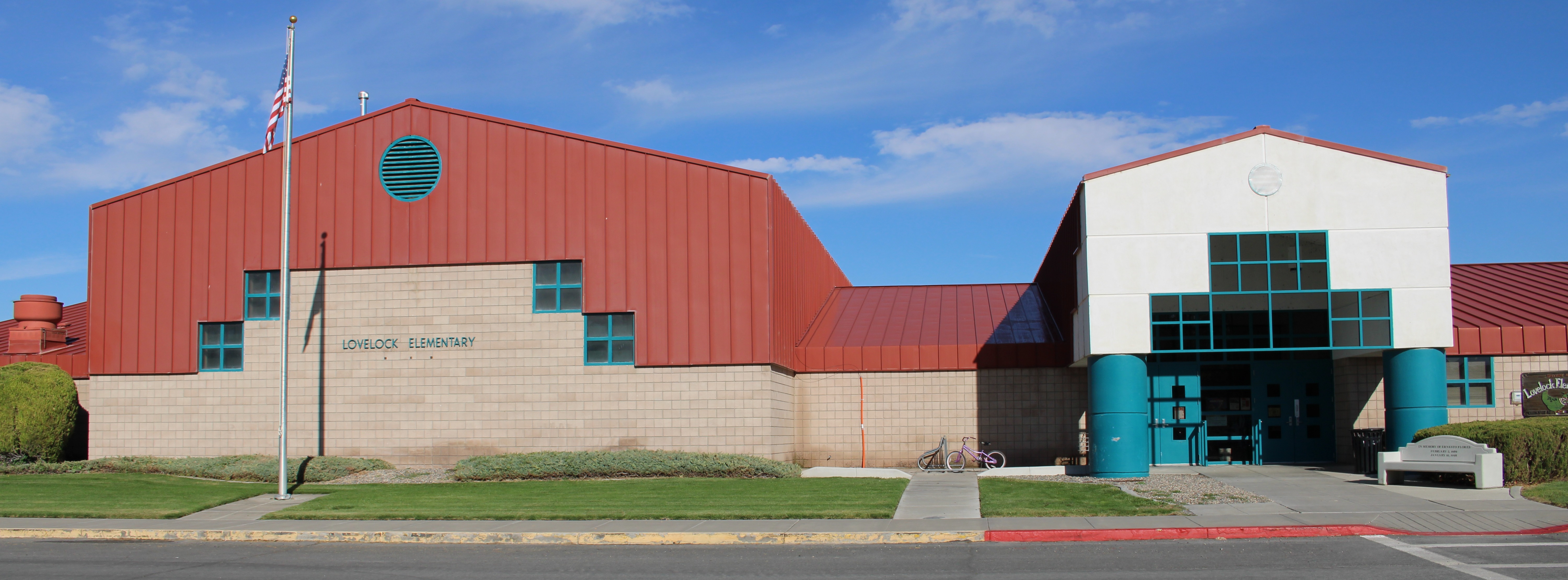 A building with a red roof and white walls. It has arched windows, a blue door, and a flagpole.