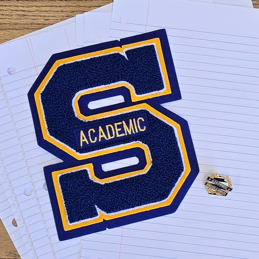 Image of a blue S with yellow trim emblazoned with the word Academic; given to students to honor academic excellence