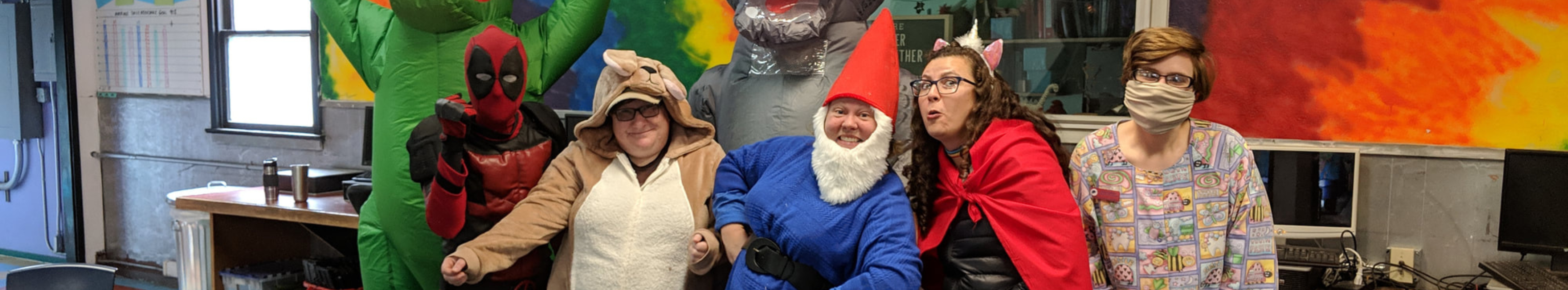 Teachers and Staff dressed up in costumes smiling and posing for a picture