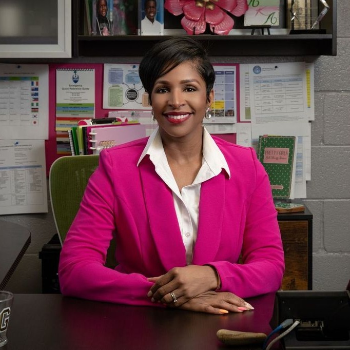 principal in pink jacket at desk