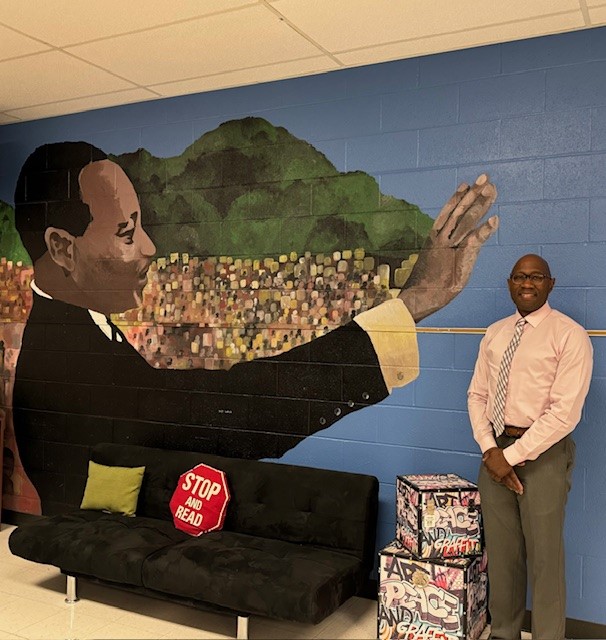 Photo of new Principal Clifton Woodley standing next to mural of Dr. King