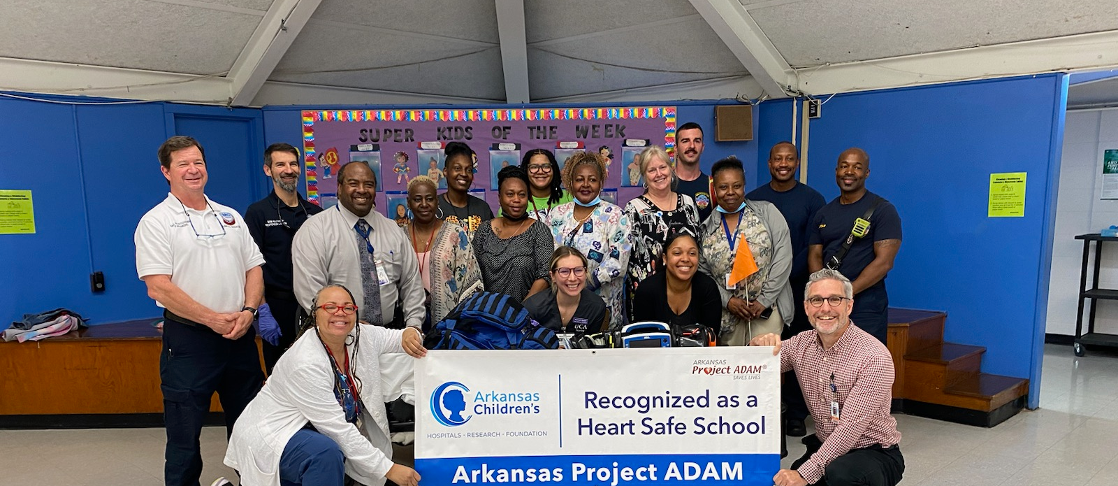 staff holding a sign that says Arkansas Children's Recognized as a Heart Safe School Arkansas Project ADAM