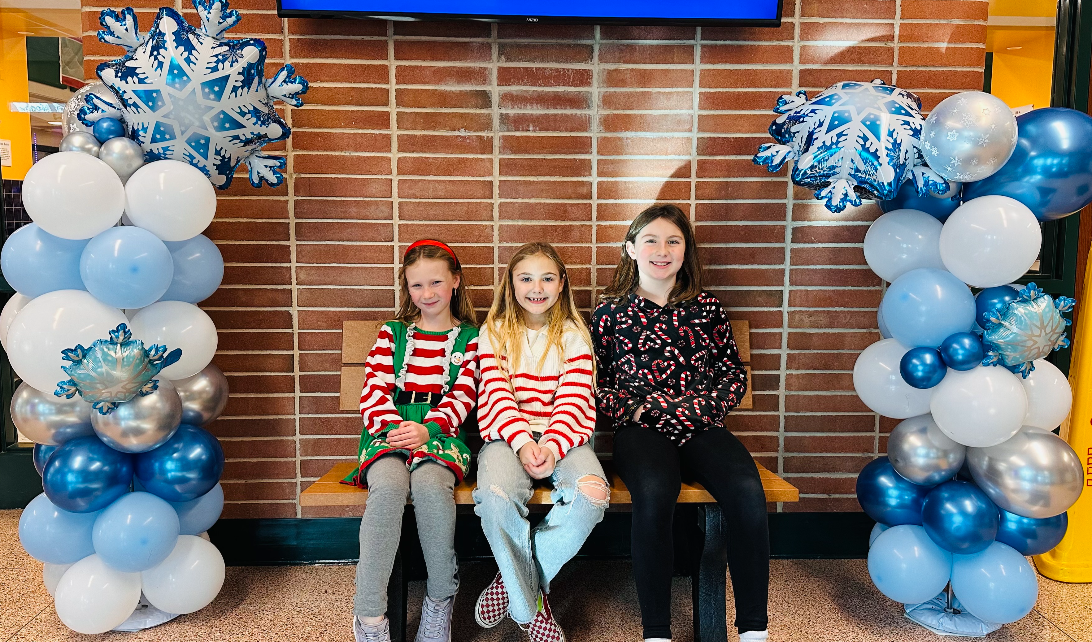 Three girls sit on a bench framed by winter balloons