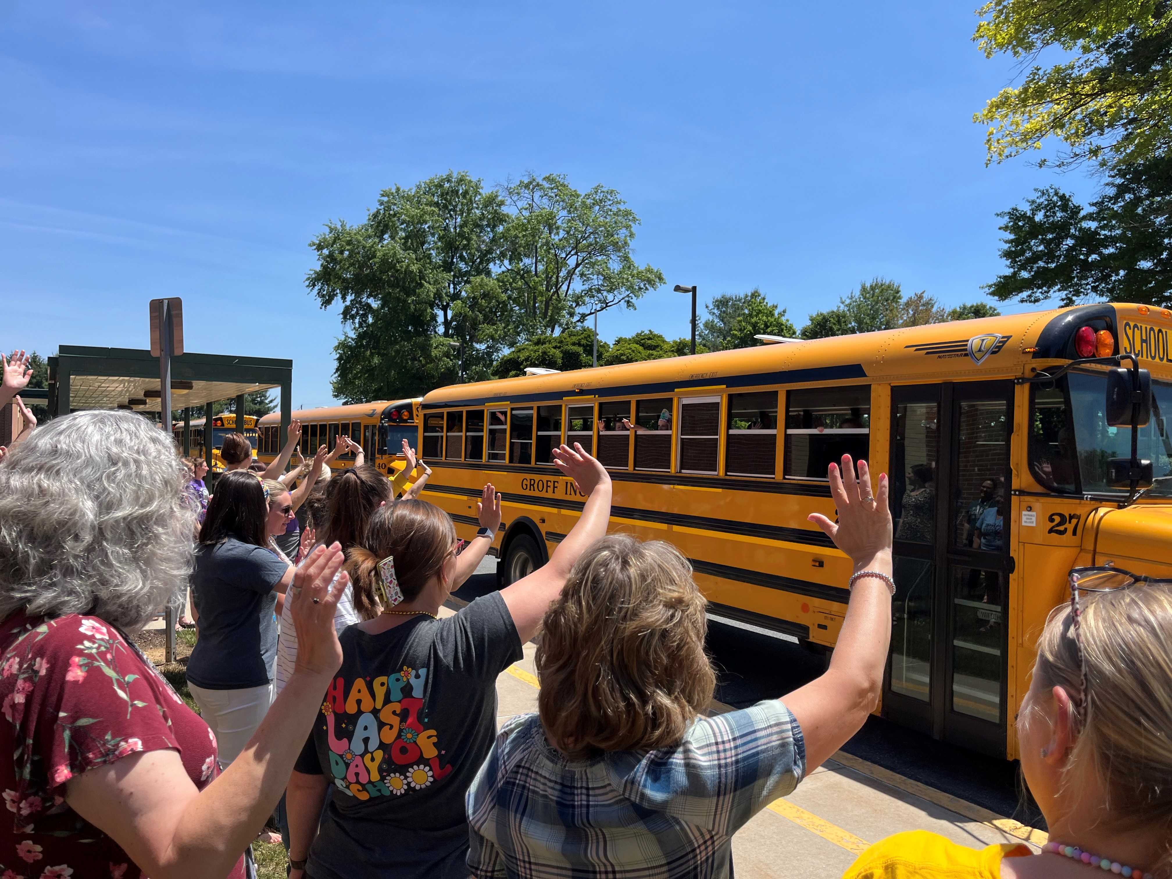 teachers and staff wave goodbye to students on buses