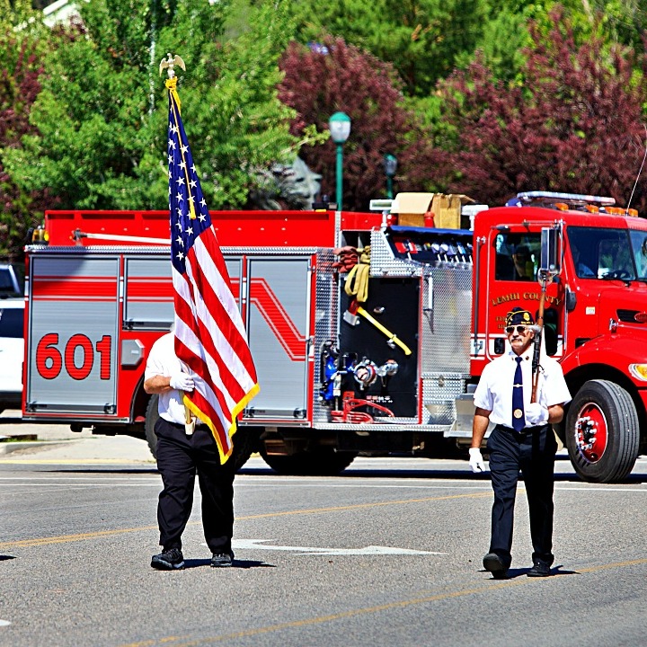 Three uniformed men marching in the street in front of a fire truck
