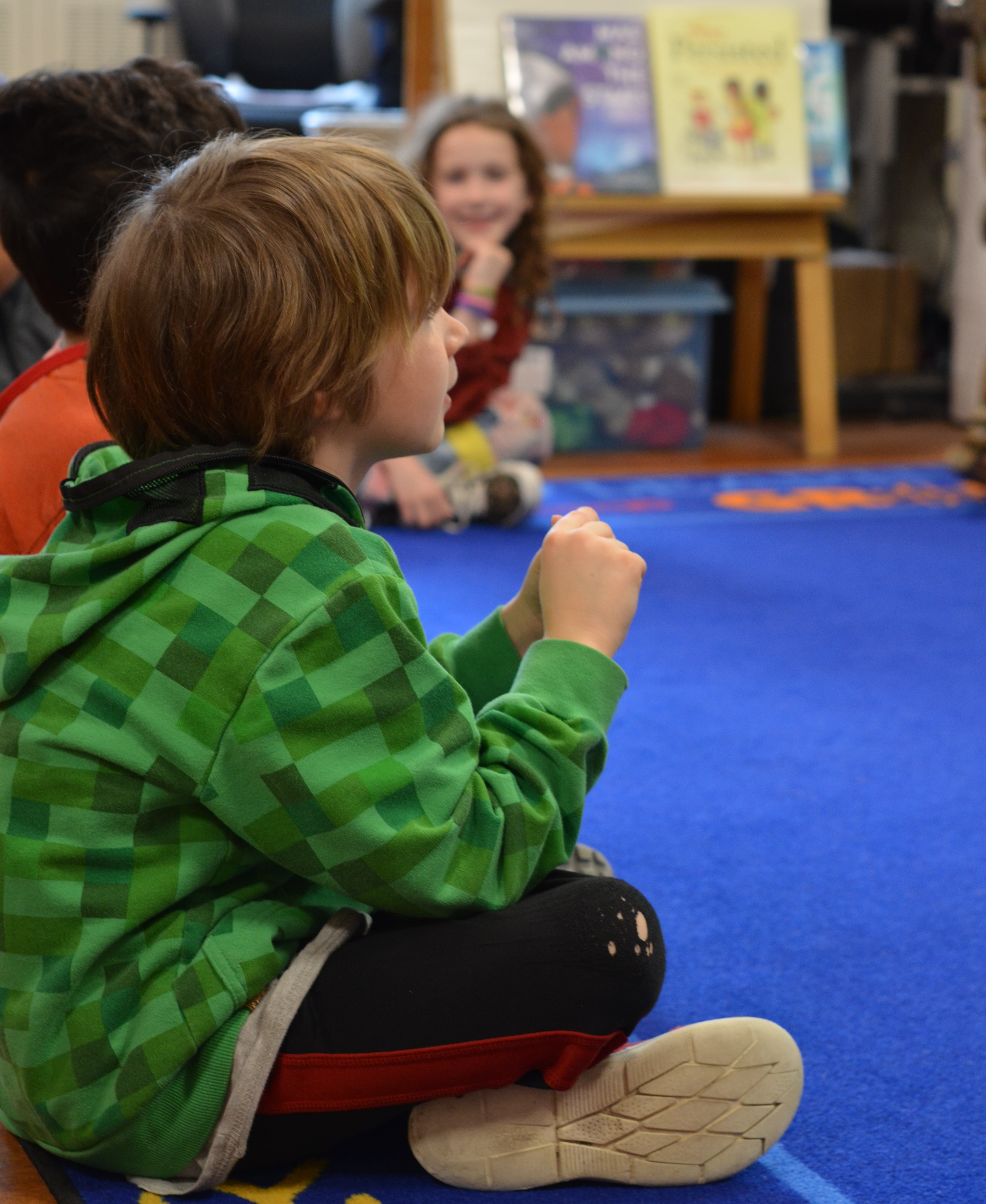 young boy sitting on classroom carpet looking at the teacher