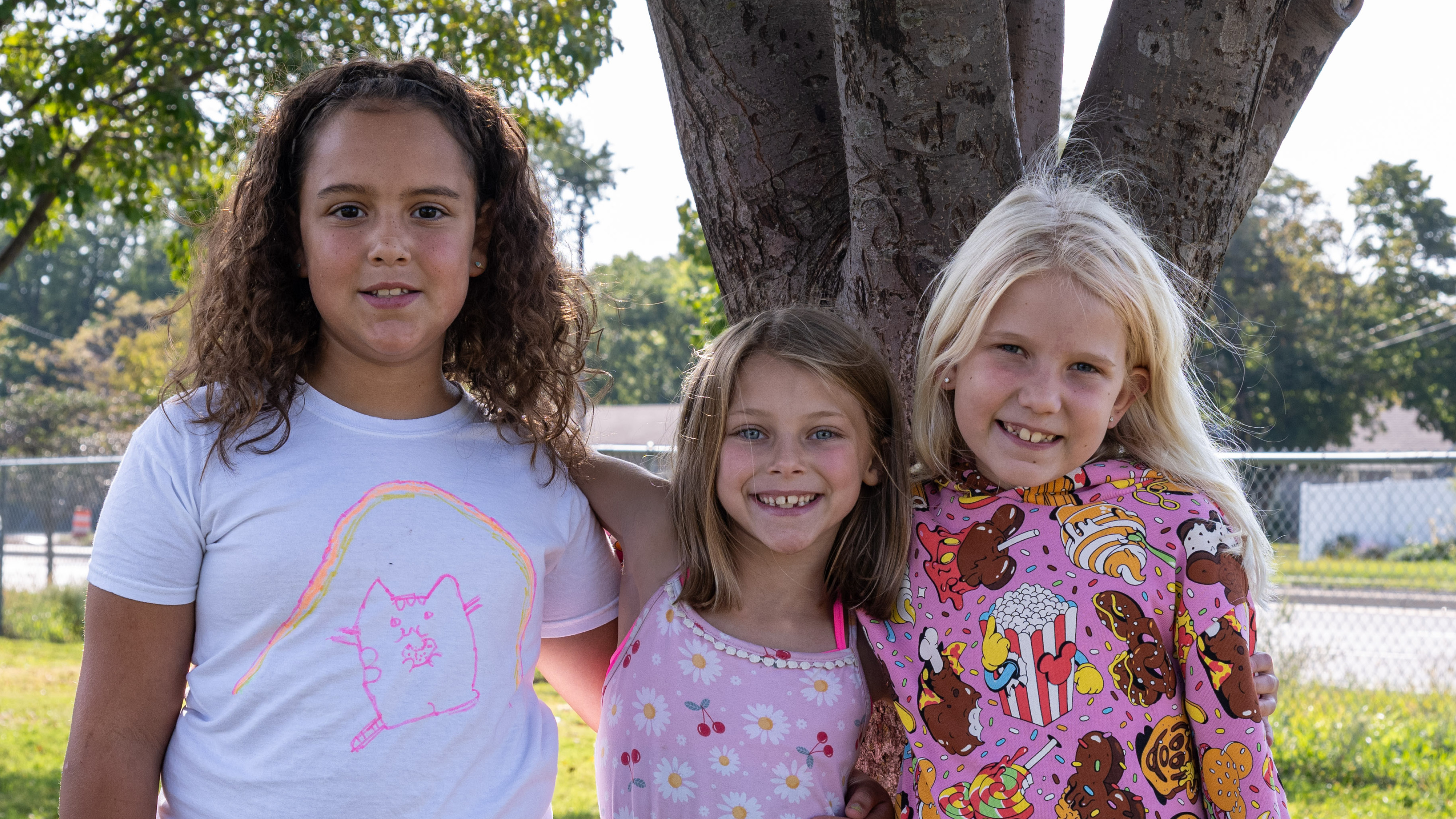 Three girls pose by a tree at recess