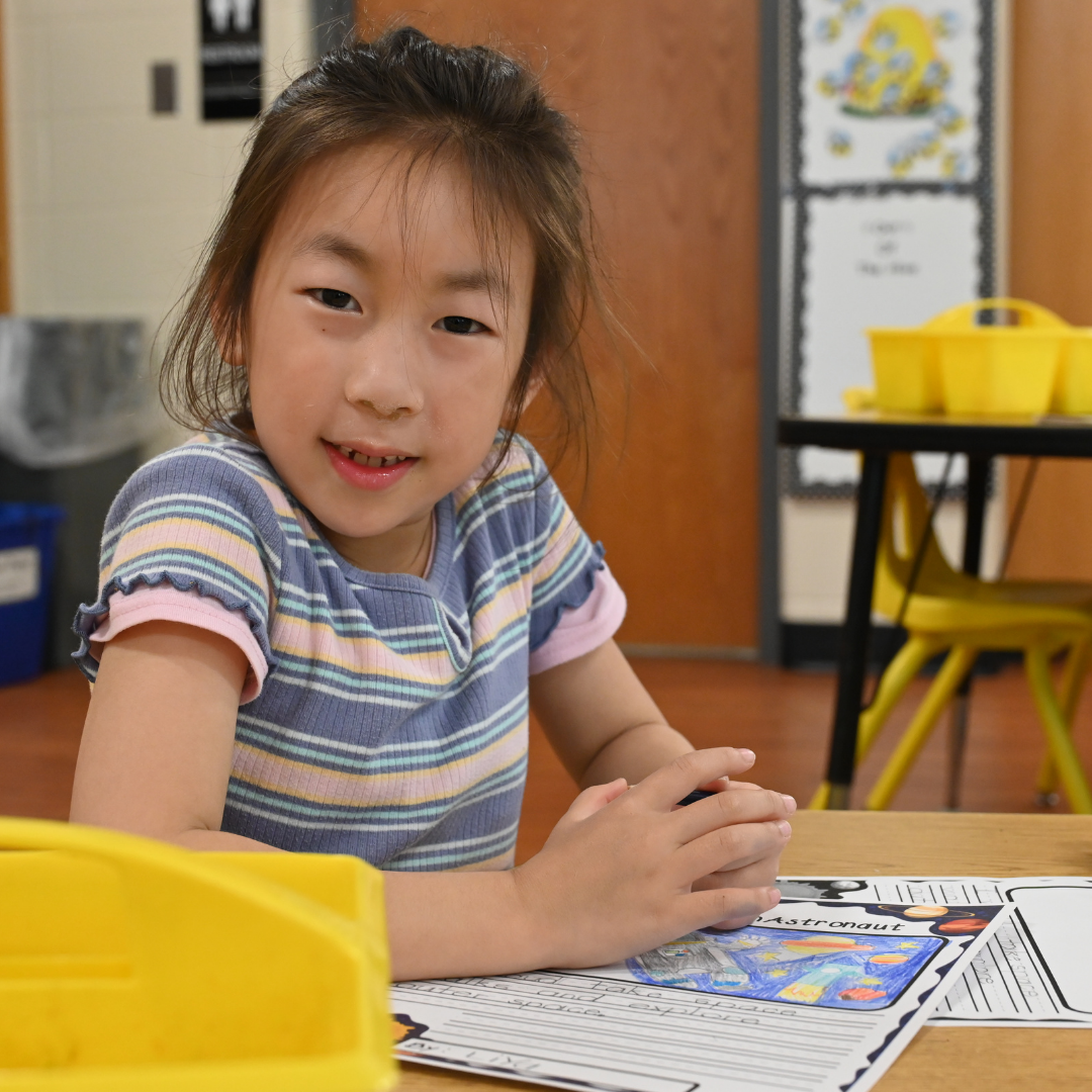 Student working on a science activity at the table smiling at the camera