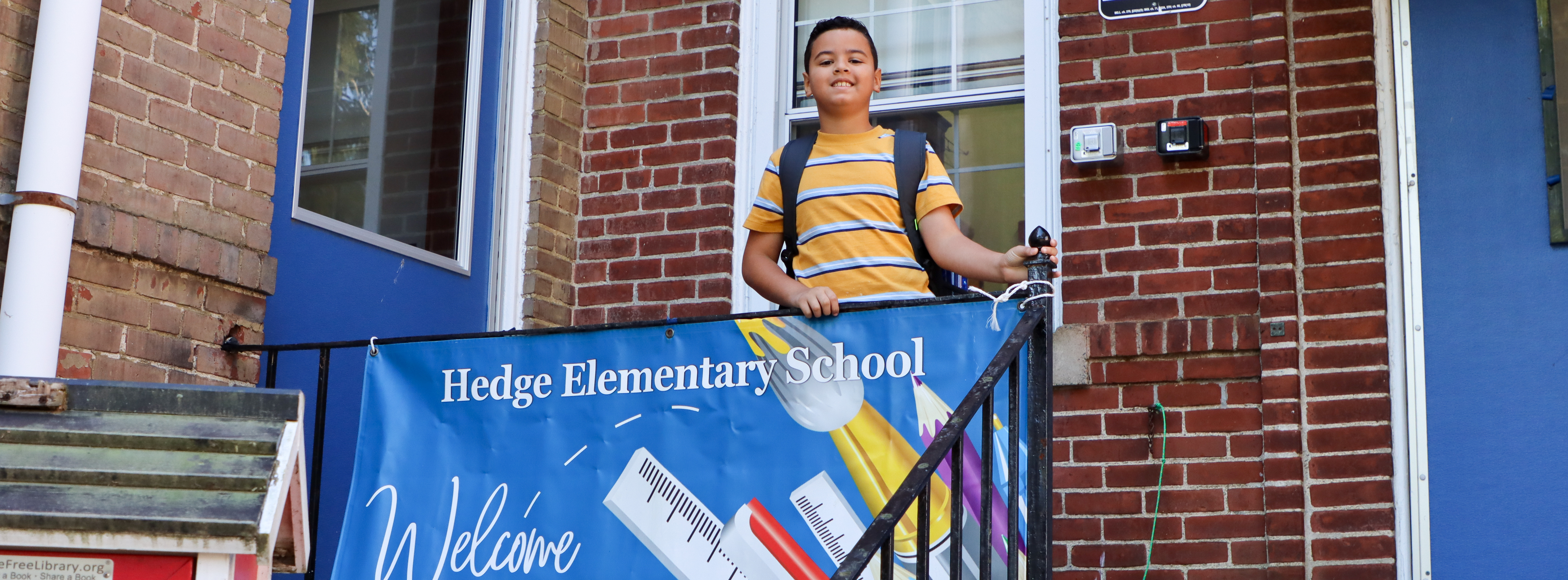 Student standing in front of a Hedge Elementary School sign.