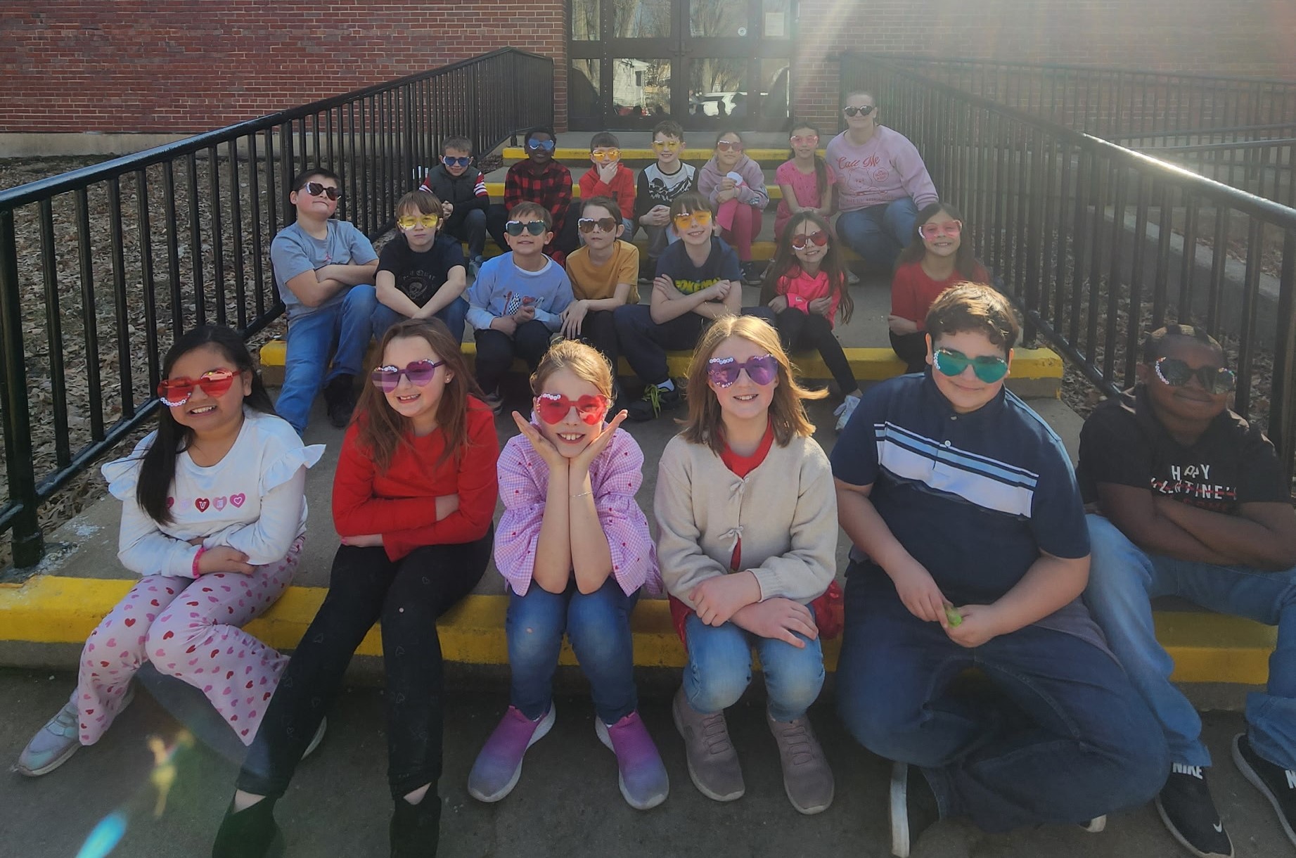 Students in Mrs. Quanstrom's class sitting on steps outside of Lincoln school, all wearing  heart shaped sunglasses