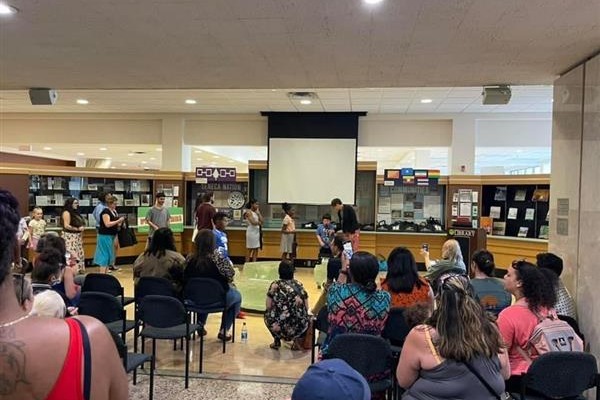 Arts Department photo- People gathered in a library. A young student is speaking to the audience of people