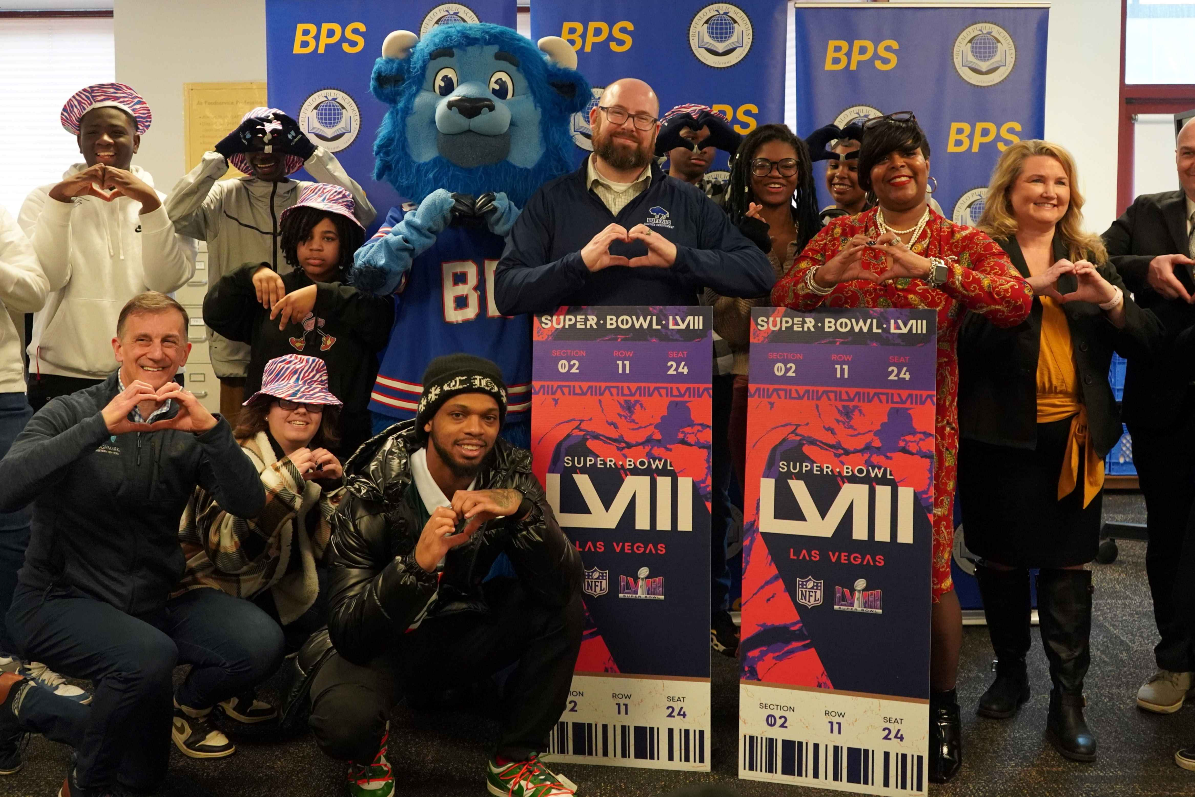 James Damon Accepting Super Bowl LVII tickets from Damar Hamlin at Emerson High School. Students and staff are pictured making heart signs with their hands.  
