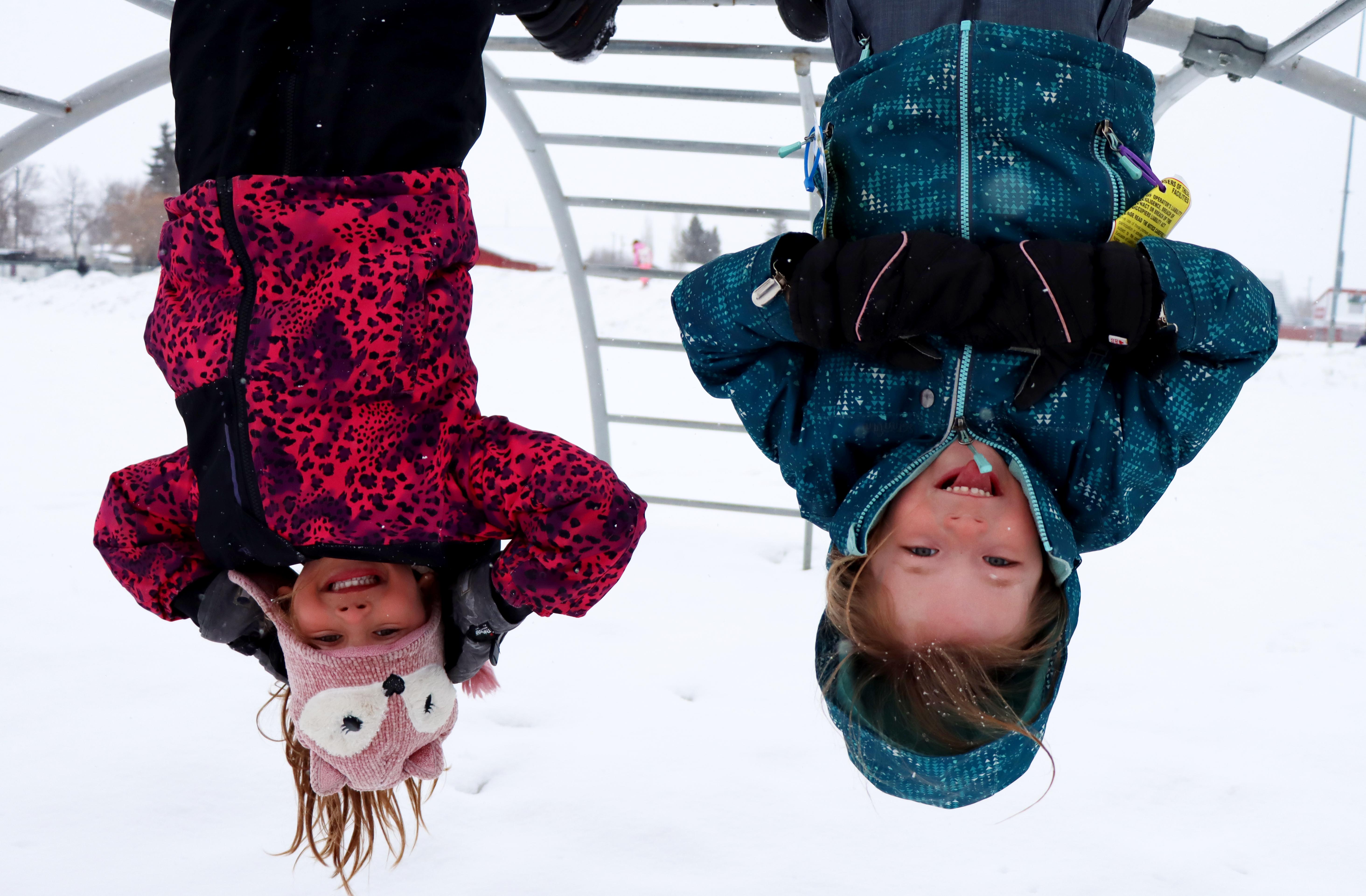 Little girls hanging upside down on monkey bars in winter