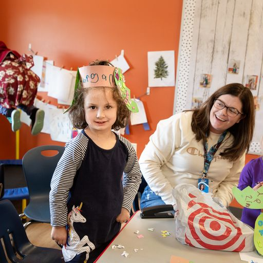 Preschool staff member smiling at a female preschool student wearing her crown.