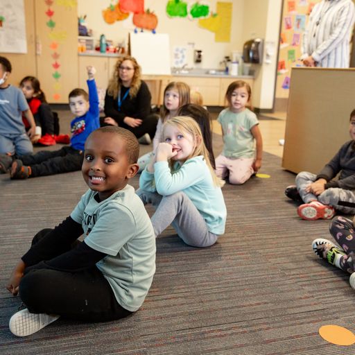 Preschool students sitting on the floor smiling at the camera.