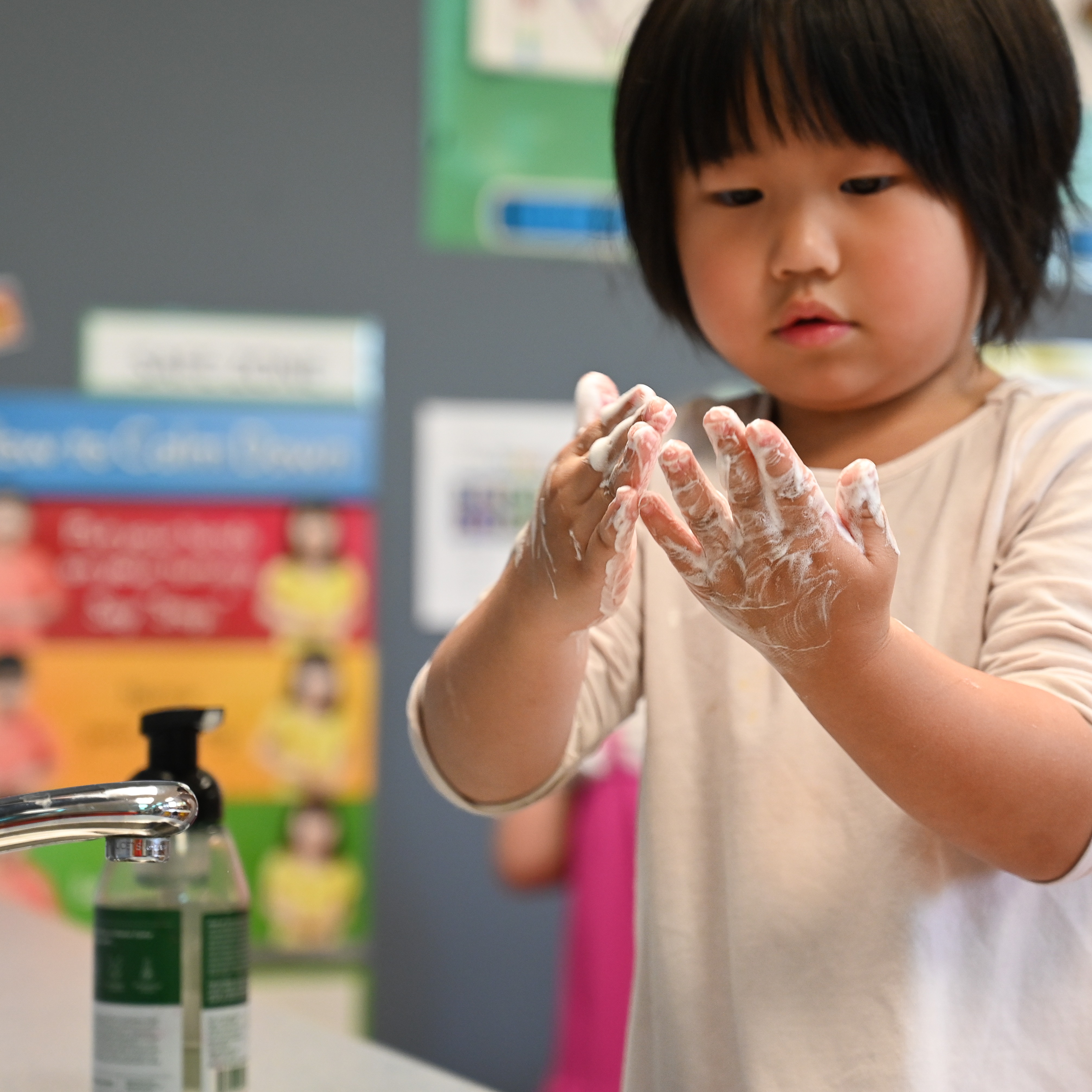 Student washing their hands in the sink and holding their hands up to their face with soapy bubbles on their hands.