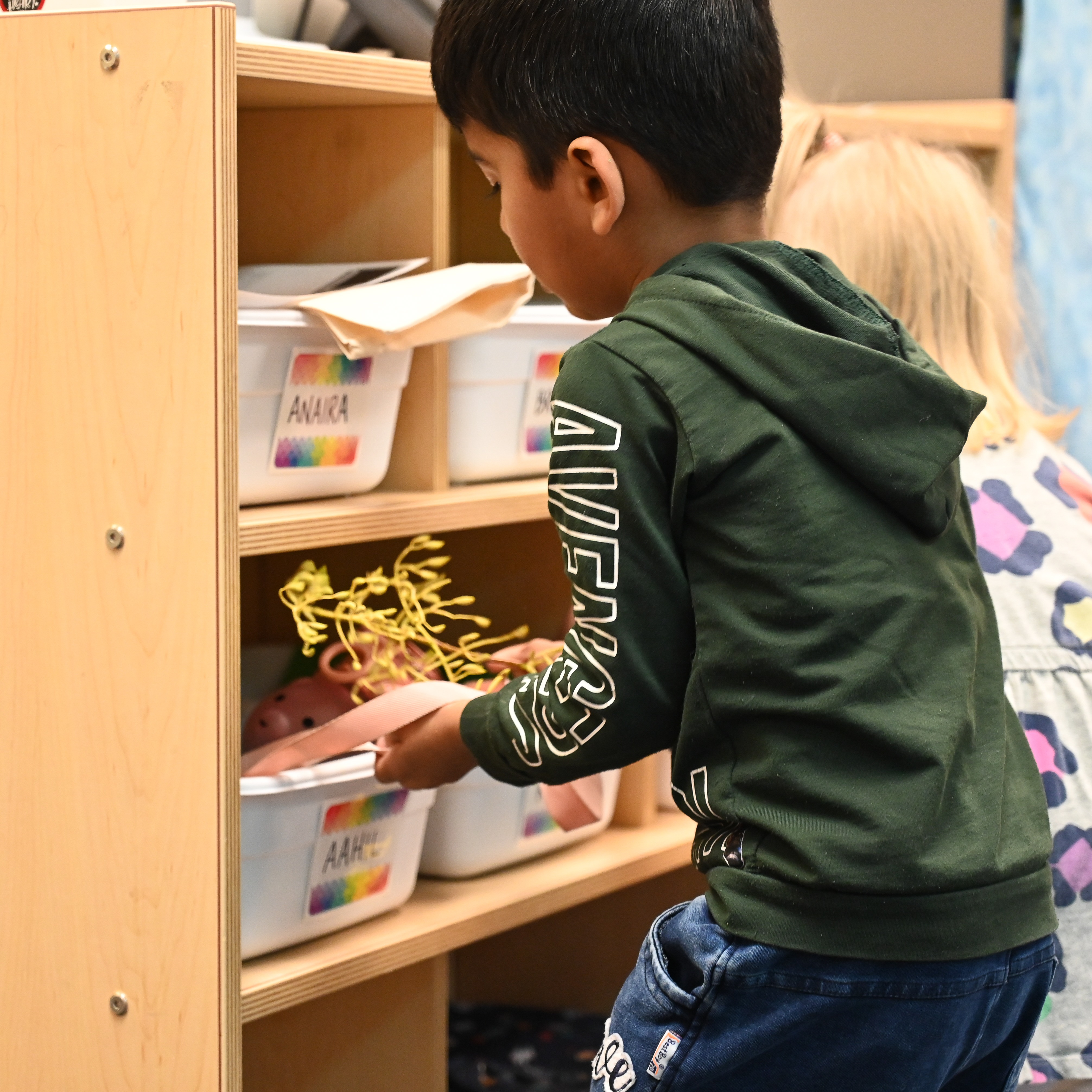 Students putting their belongings in classroom bins