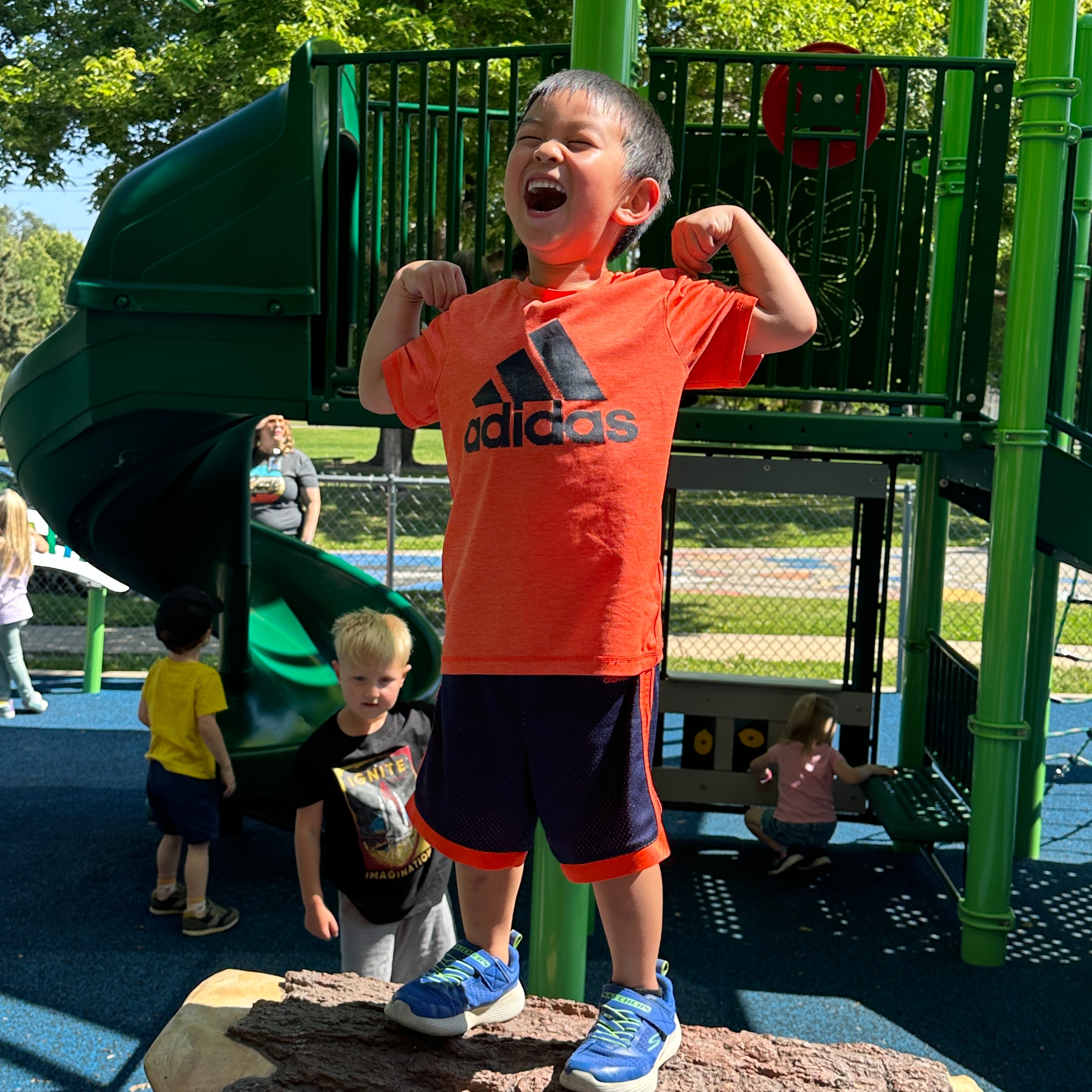 Student on top of log at Northrop playground with arms up "like look at me I am strong"