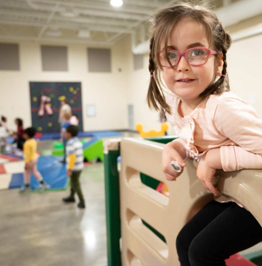 Female preschool student holding on to a climber in the gym