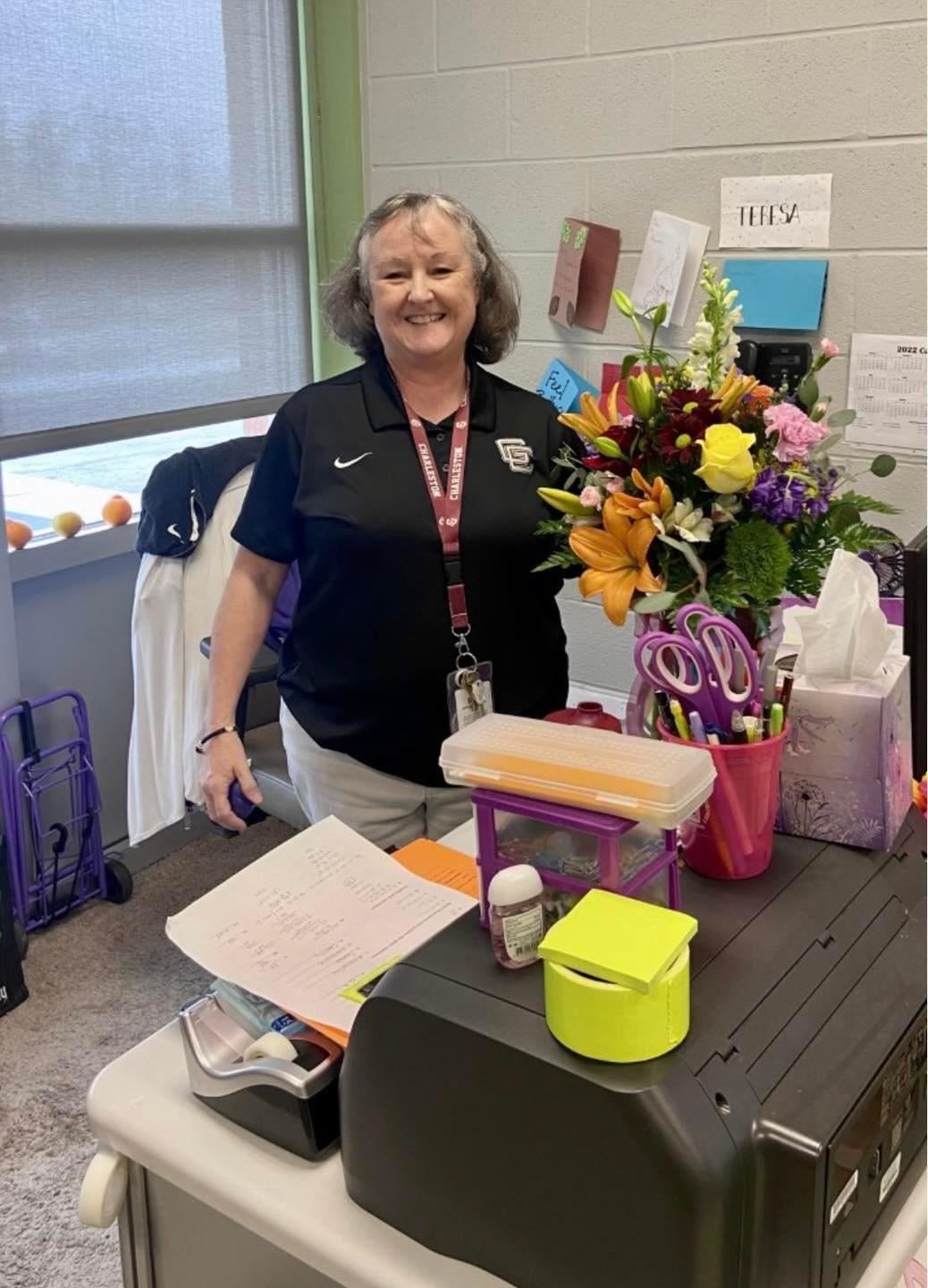 Mrs. Borgardts standing behind her desk smiling next to a bouquet of flowers