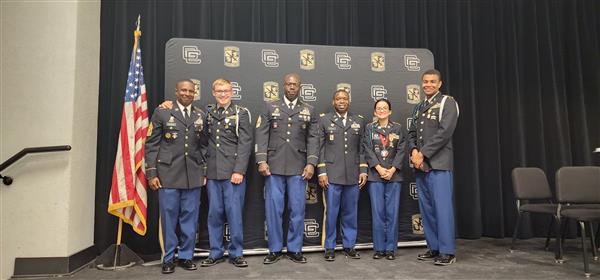 six people in uniform posing next to an American flag