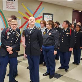 a line of JROTC students in a hallway. The two students at the front of the line are smiling for the camera