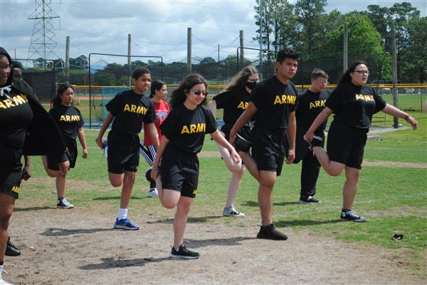 students outdoors in rows wearing matching Army shirts stretching their legs