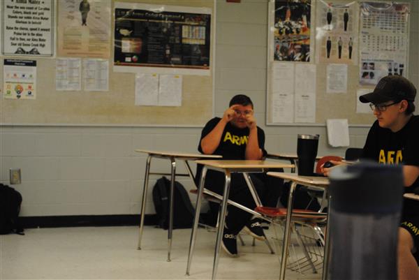 student in an army shirt holding up his hands as if he were photographing the photographer