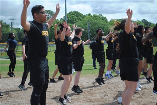 students outdoors in rows wearing matching Army shirts doing jumping jacks