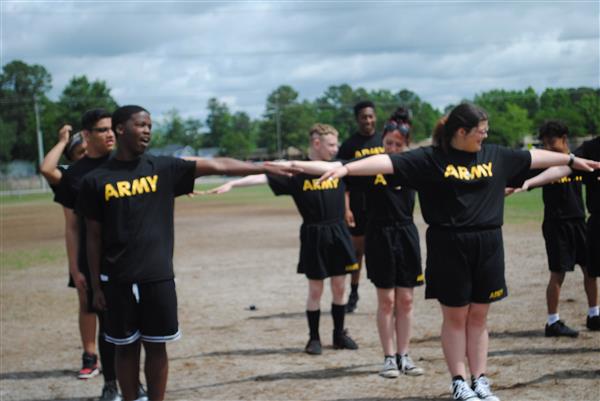 students outdoors in rows wearing matching Army shirts holding their arms outstretched