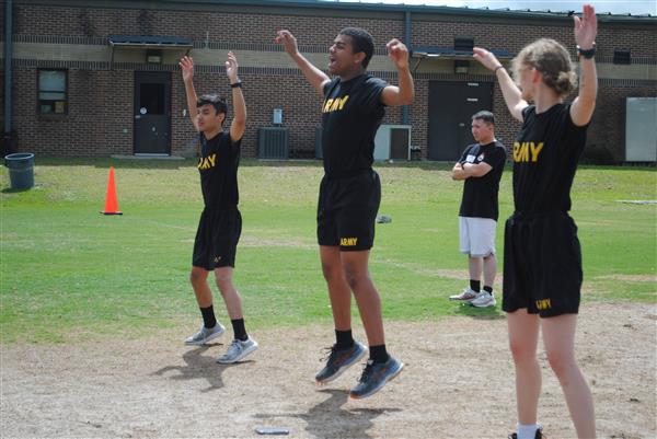 students outdoors in rows wearing matching Army shirts doing jumping jacks